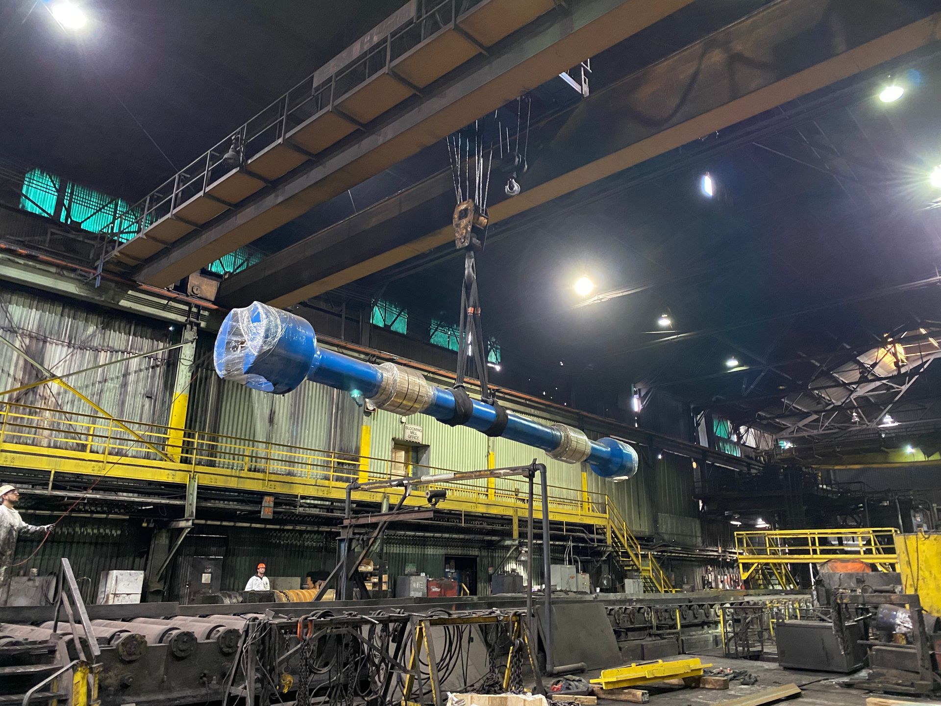 A large blue pipe is being lifted by a crane in a factory.