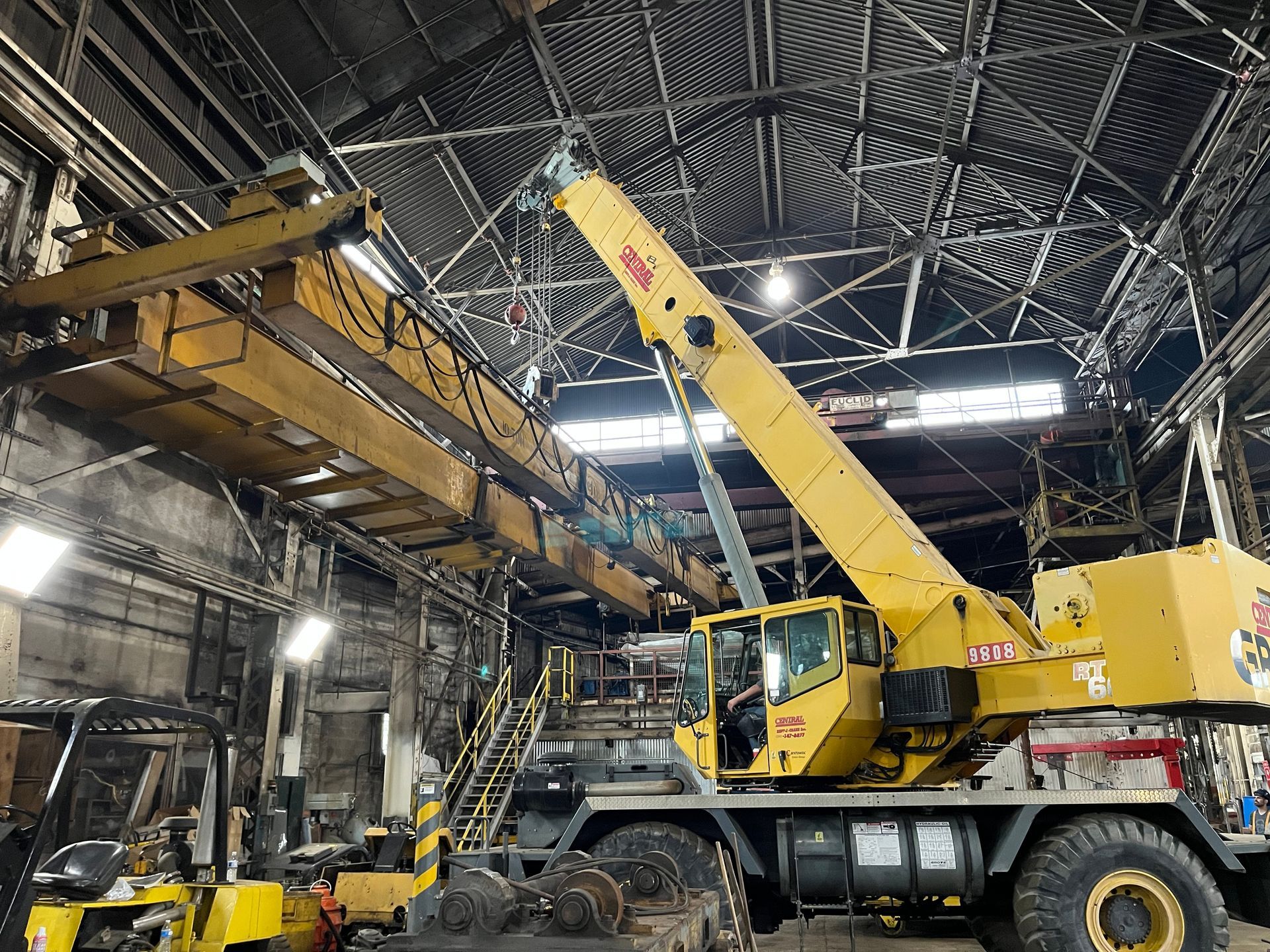 A large yellow crane is sitting in a warehouse next to a forklift.