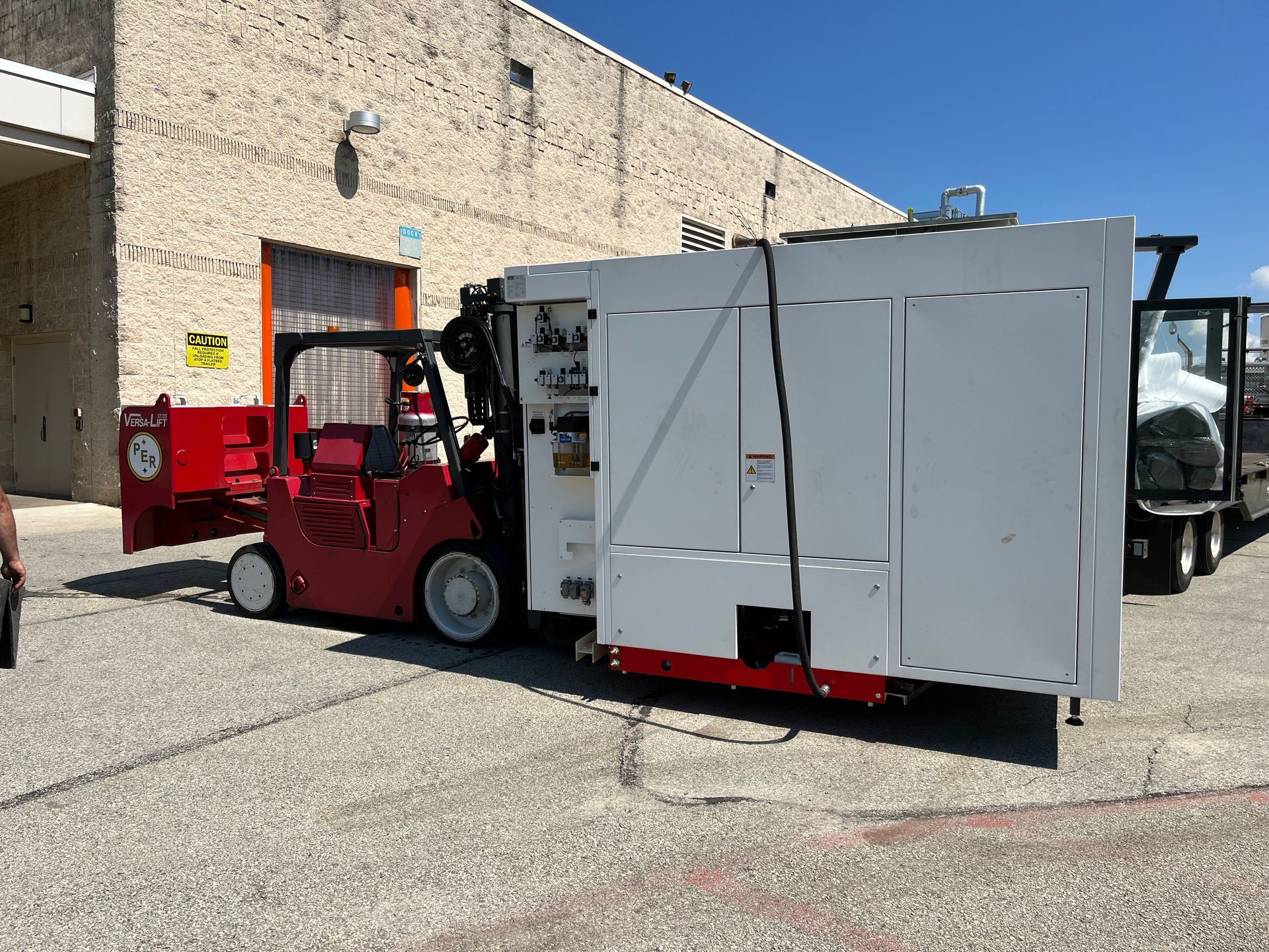 A forklift is carrying a large white box in front of a building.