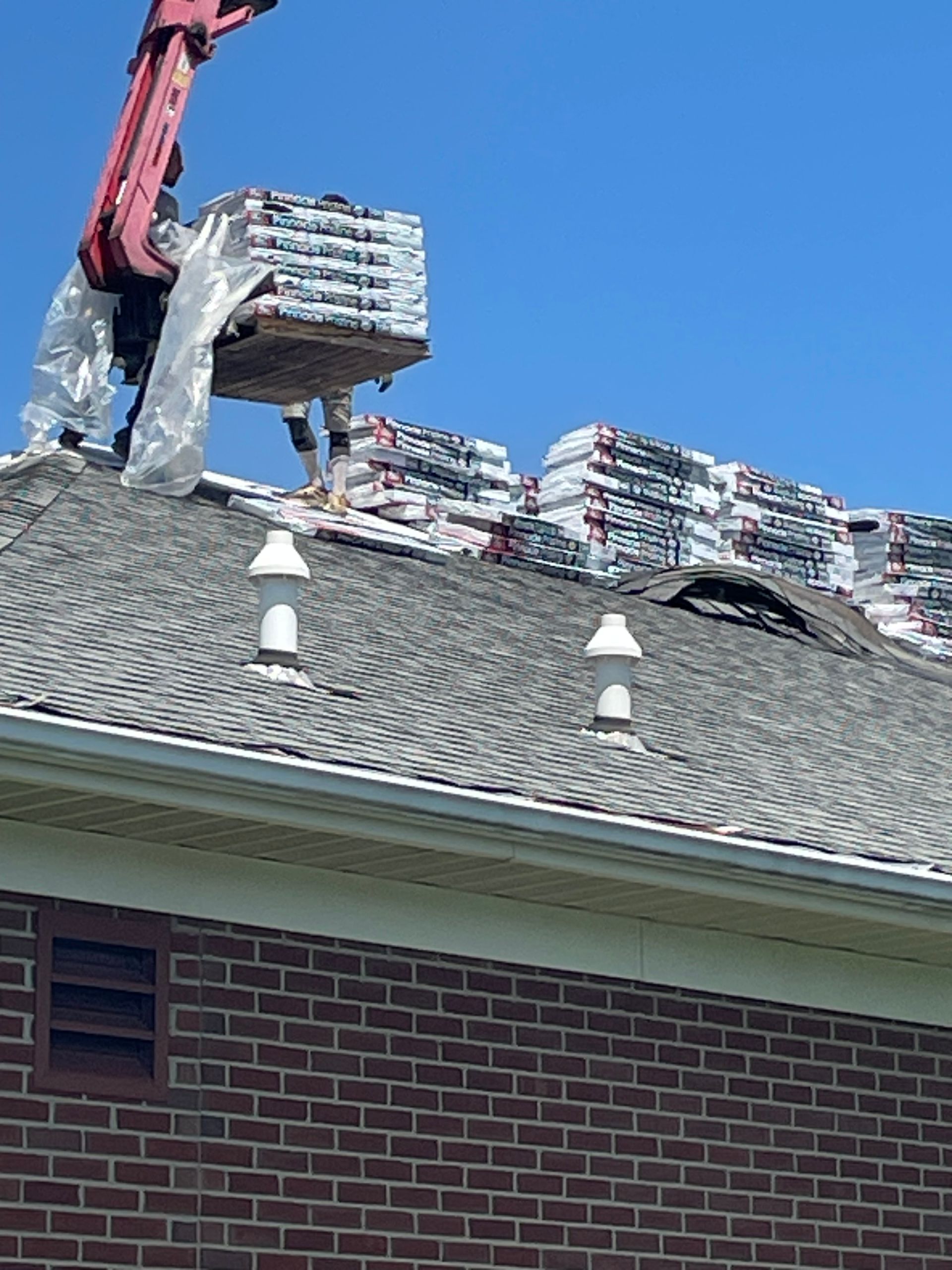Crane unloading bundled roofing materials onto a house roof during repairs