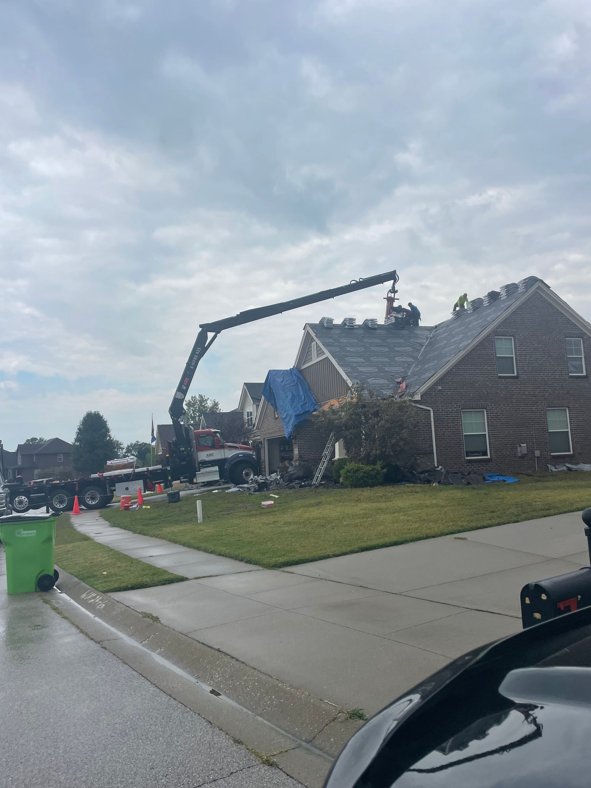 Storm damage cleanup at a house, with a crane lifting debris beside a wet suburban street.