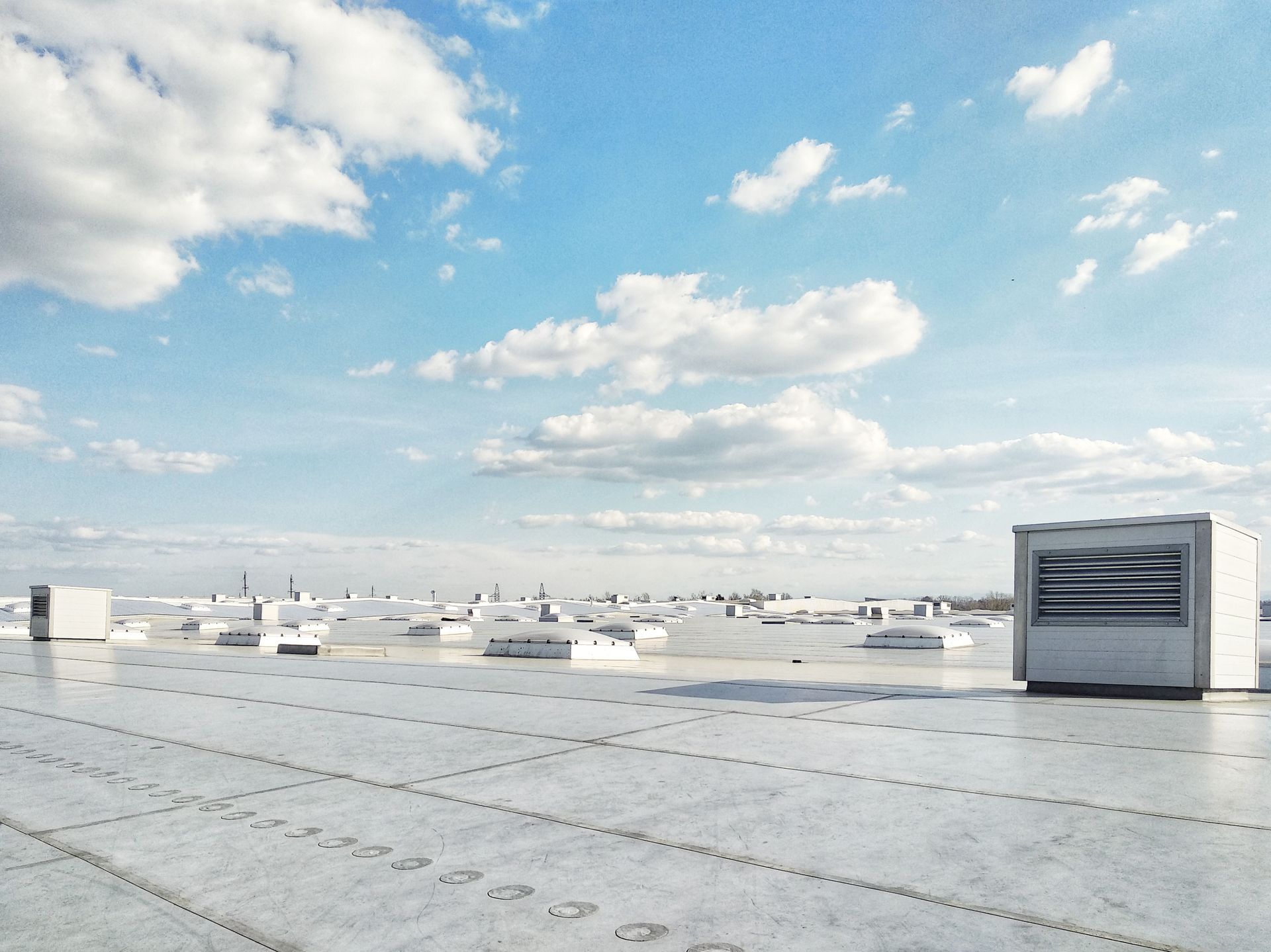 Wide rooftop with white vents under a bright blue sky and scattered clouds