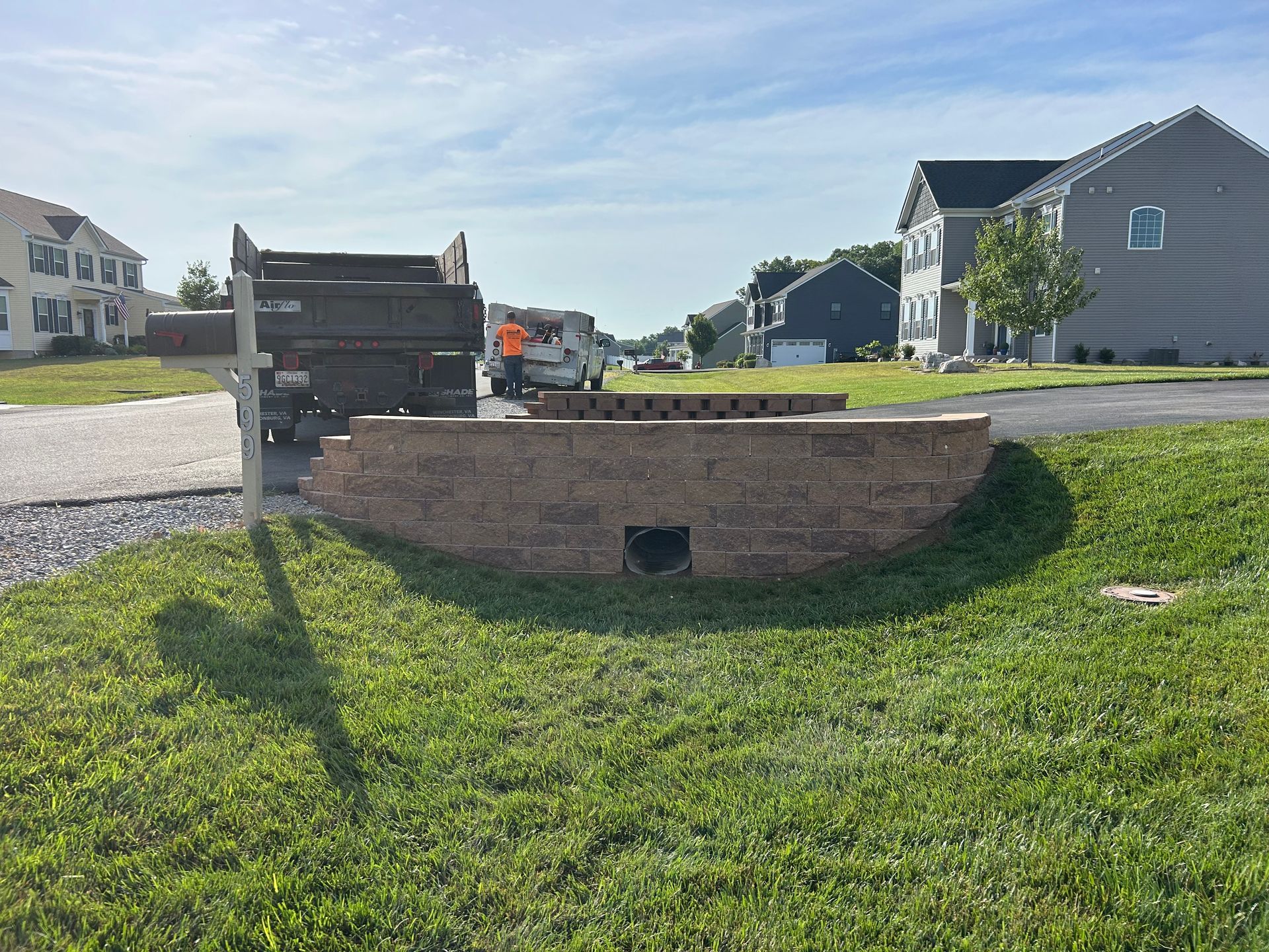 A low tan stone retaining wall sits in a grassy residential front yard, with a dark construction truck parked nearby.