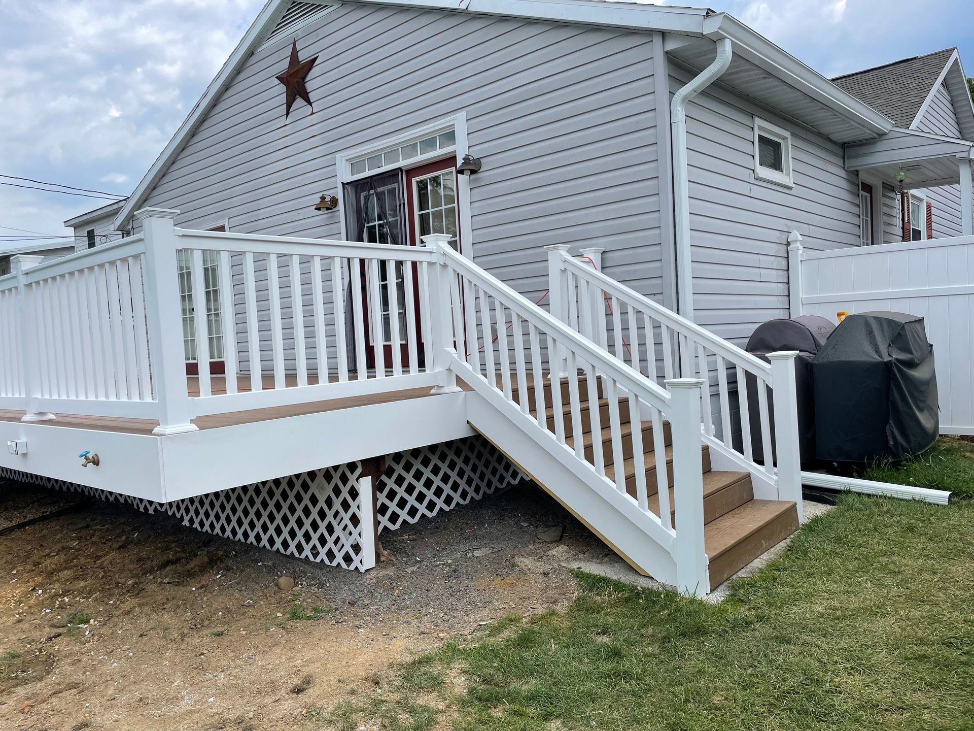 A house exterior featuring a wooden deck with white railings, a matching staircase, and white lattice skirting.