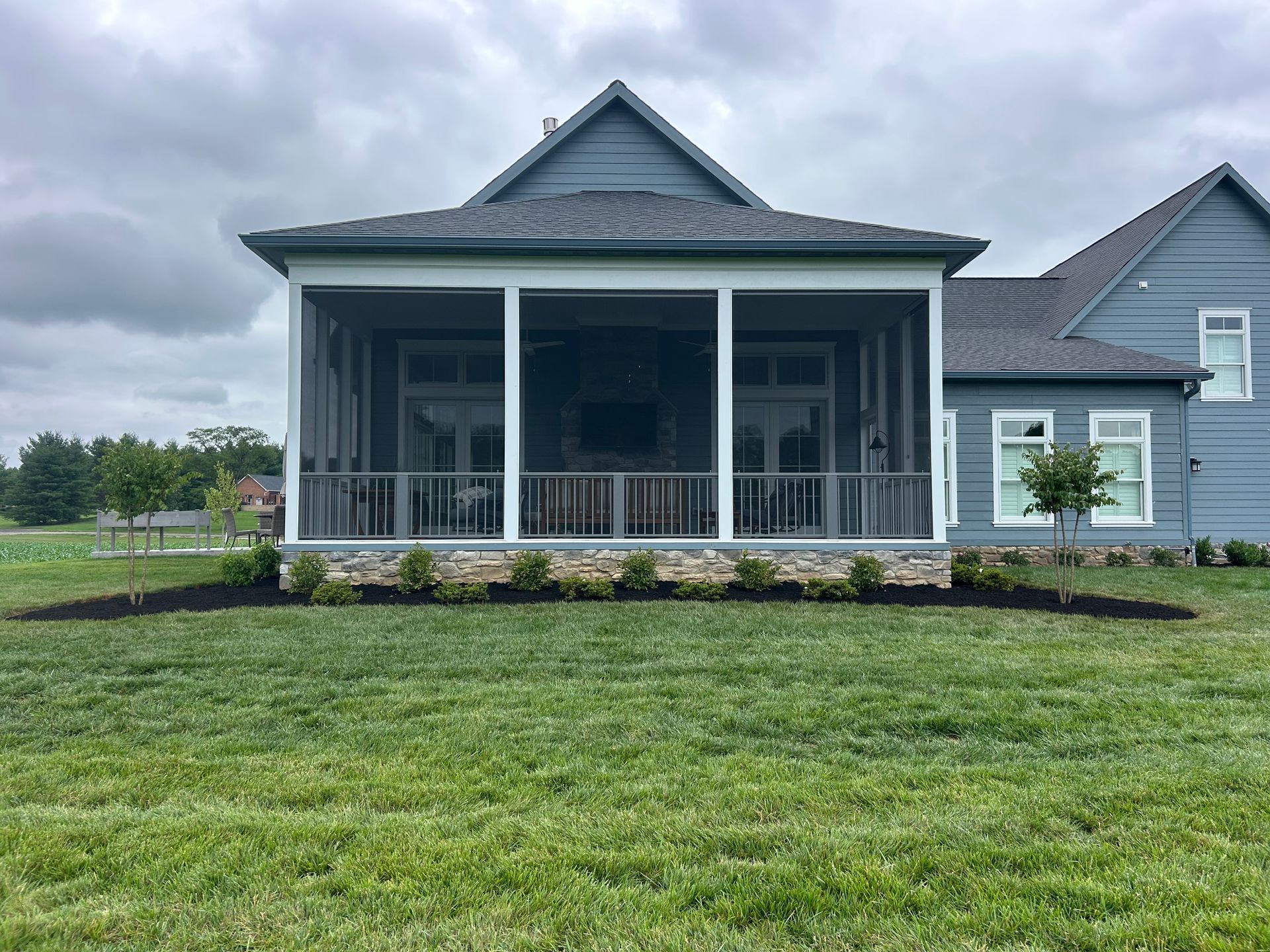A blue house with a covered, screened-in back porch, stone foundation, and a newly landscaped lawn.