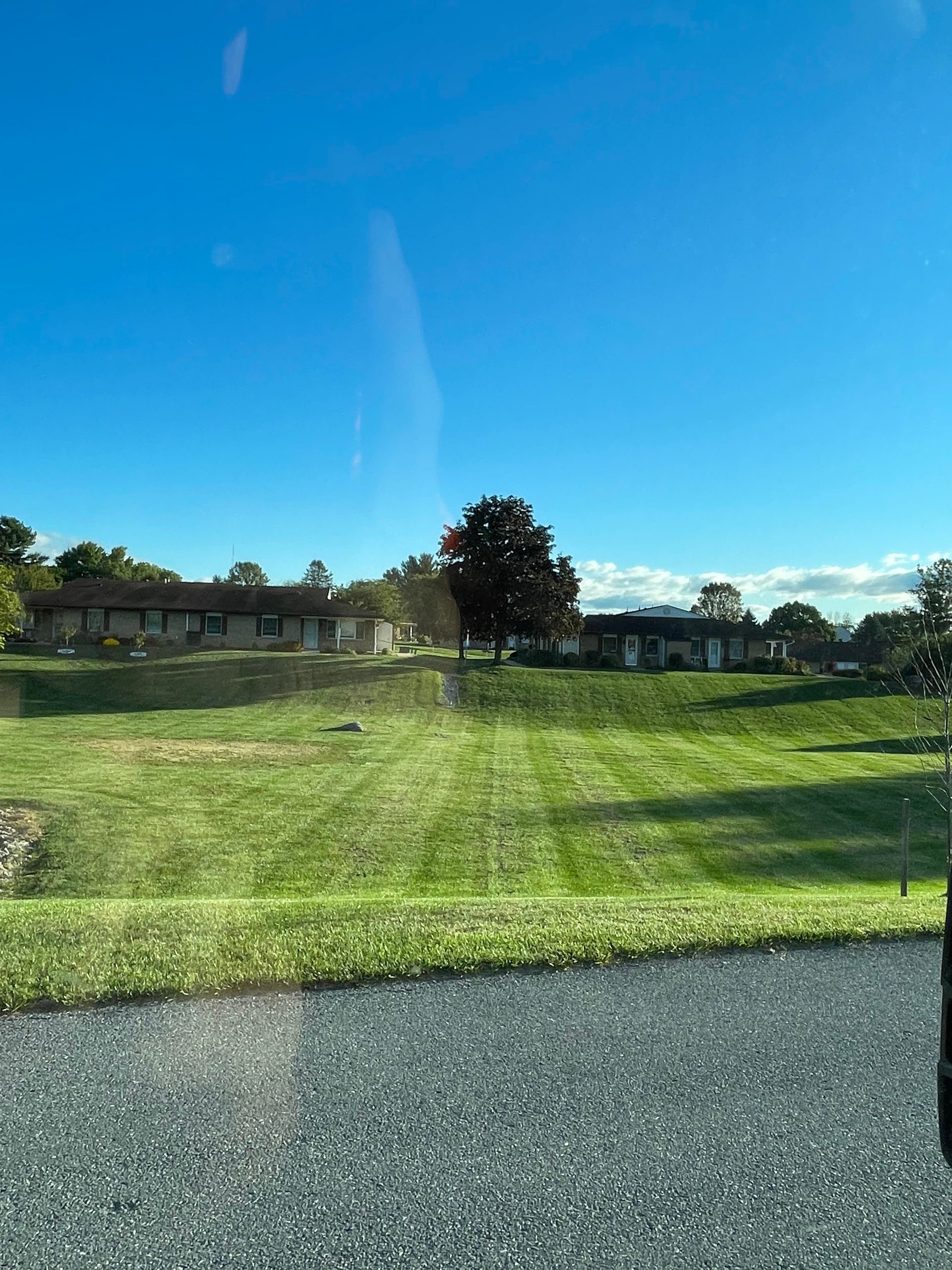 A wide, mown green lawn stretches toward two suburban houses under a bright blue sky.