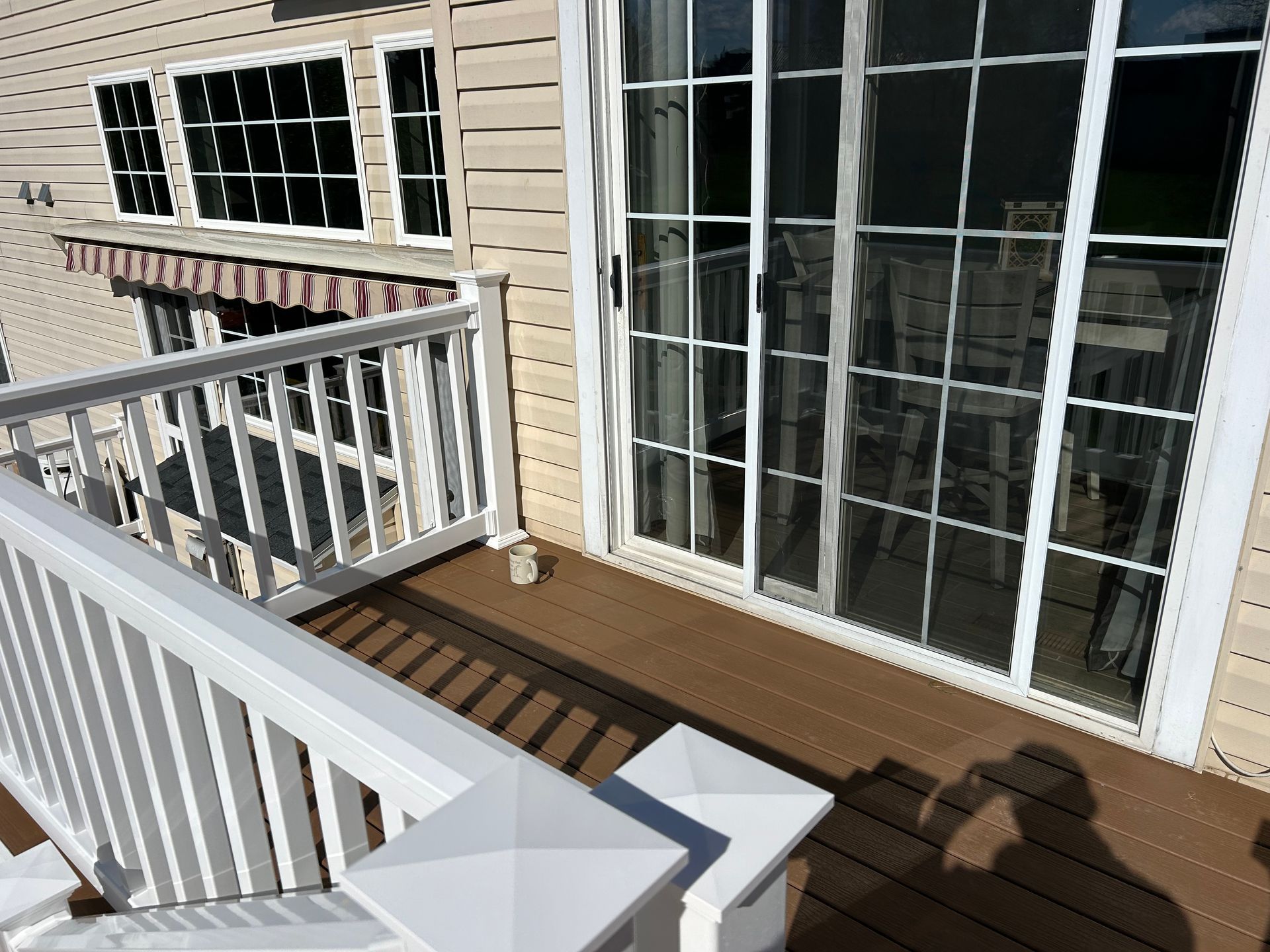 An elevated deck with brown composite boards, white railings, and a glass sliding door leading into the home.