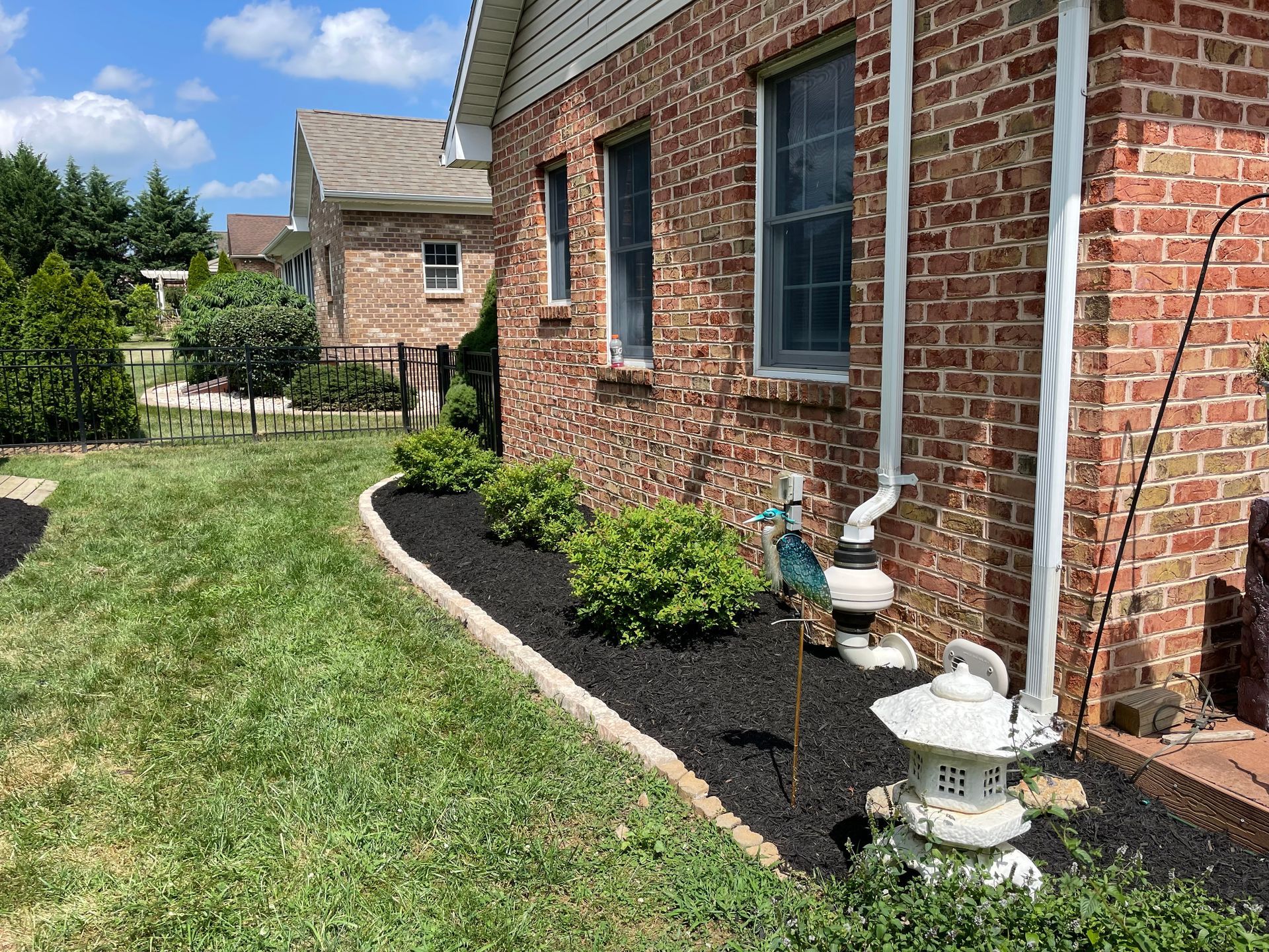 A brick house exterior with a black mulch garden bed featuring small green bushes and a decorative stone lantern.