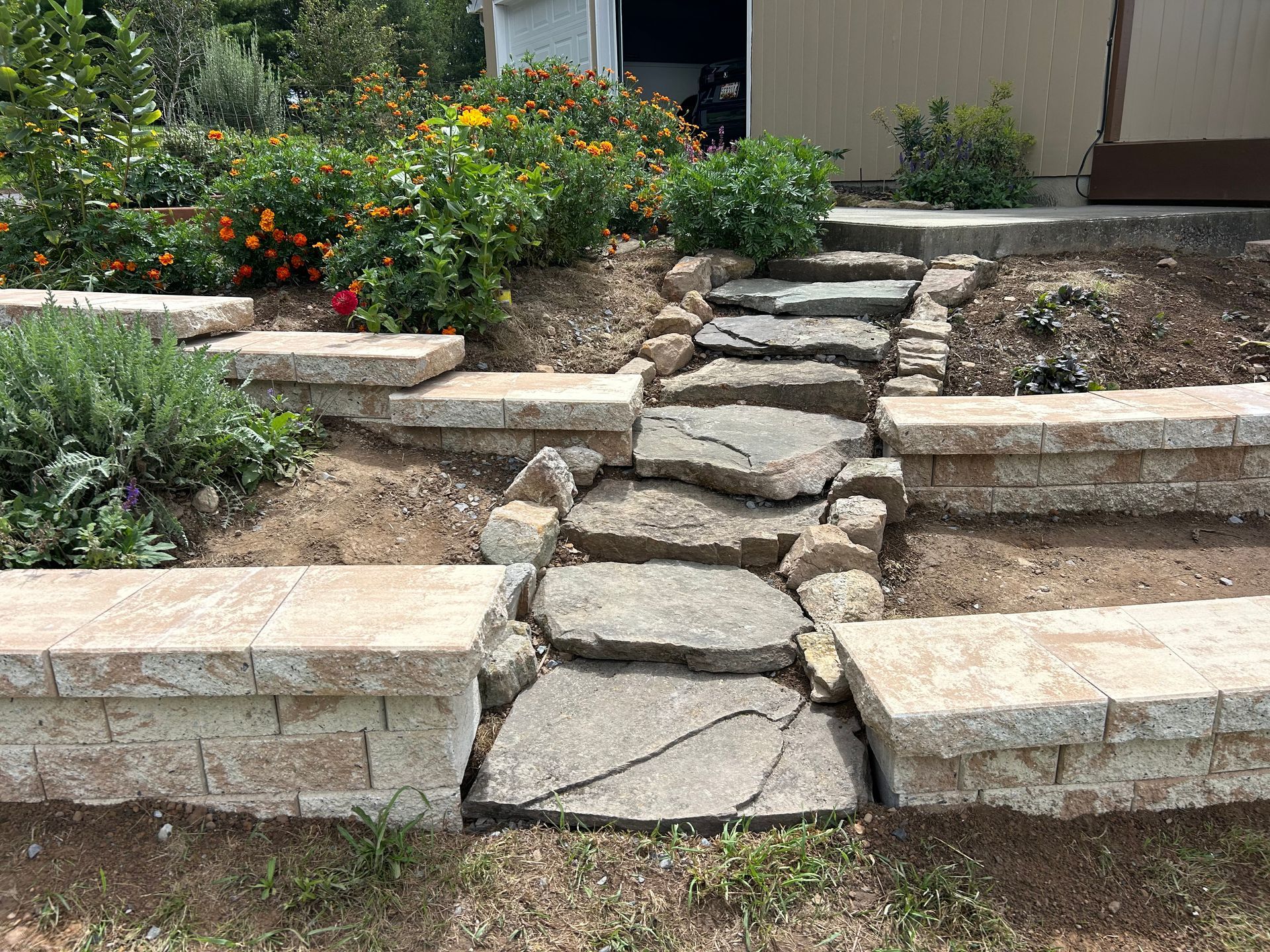 A stone staircase set between two low retaining walls, surrounded by garden beds with flowers and shrubs.