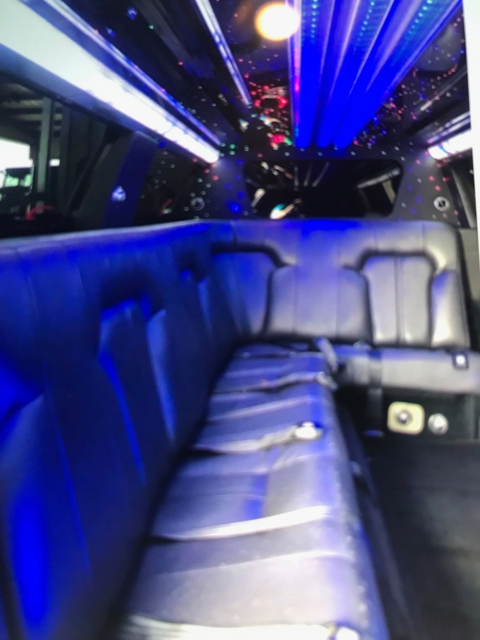 The interior of a limousine featuring dark leather bench seating, blue ambient lighting, and a starry fiber-optic ceiling.