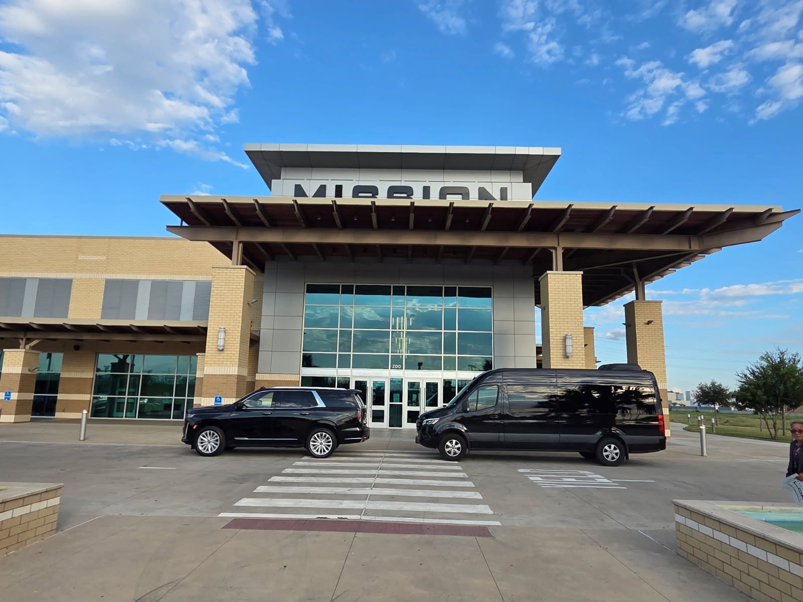 A black SUV and a black passenger van parked in front of a building with the word MISSION on the facade.