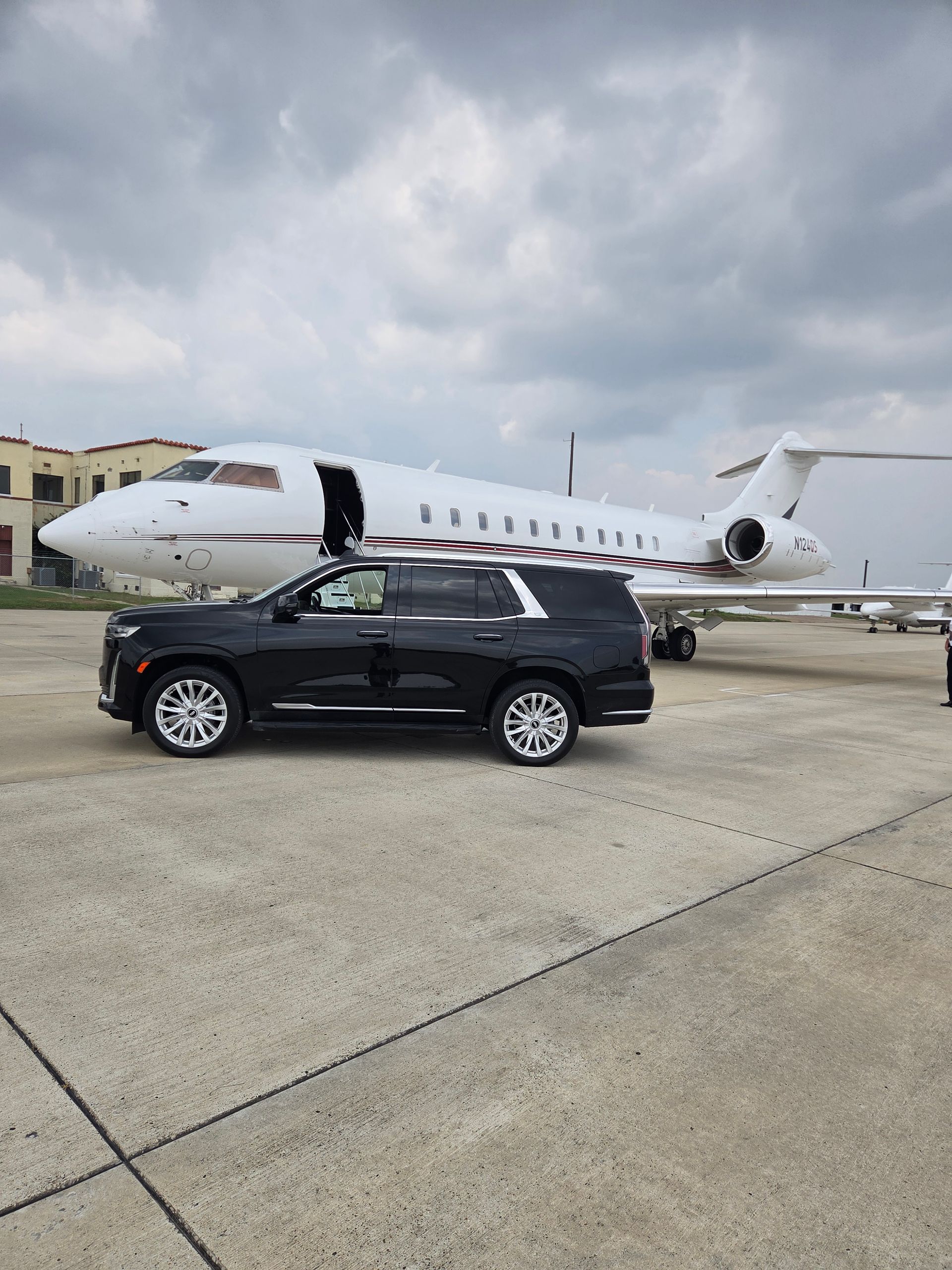 Black SUV parked in front of a white private jet on an airport tarmac under cloudy skies