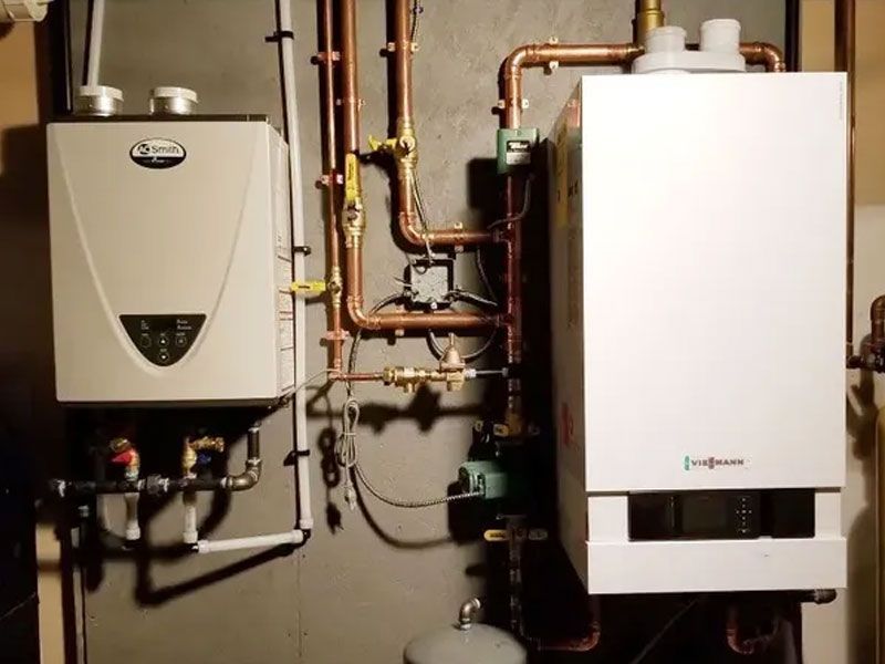 Two wall-mounted, white heating units with copper piping against a gray wall.