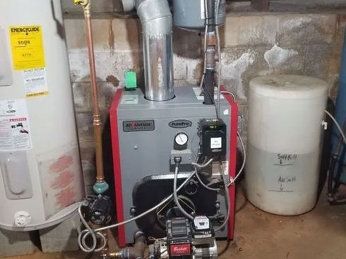 A furnace in a basement setting with a water tank and copper pipes.