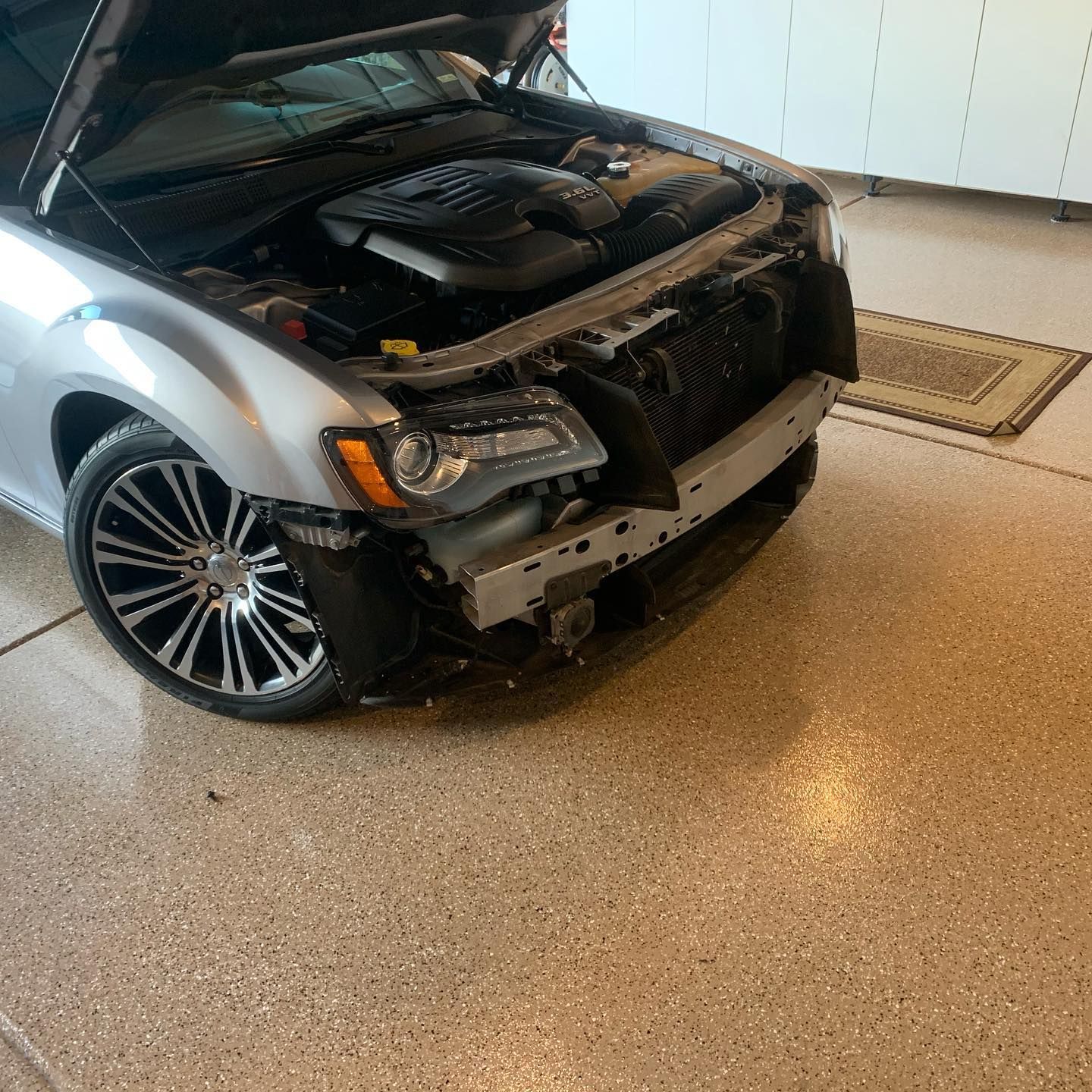 A dark-colored SUV on an asphalt road with visible front-end damage to the bumper and hood after a collision.
