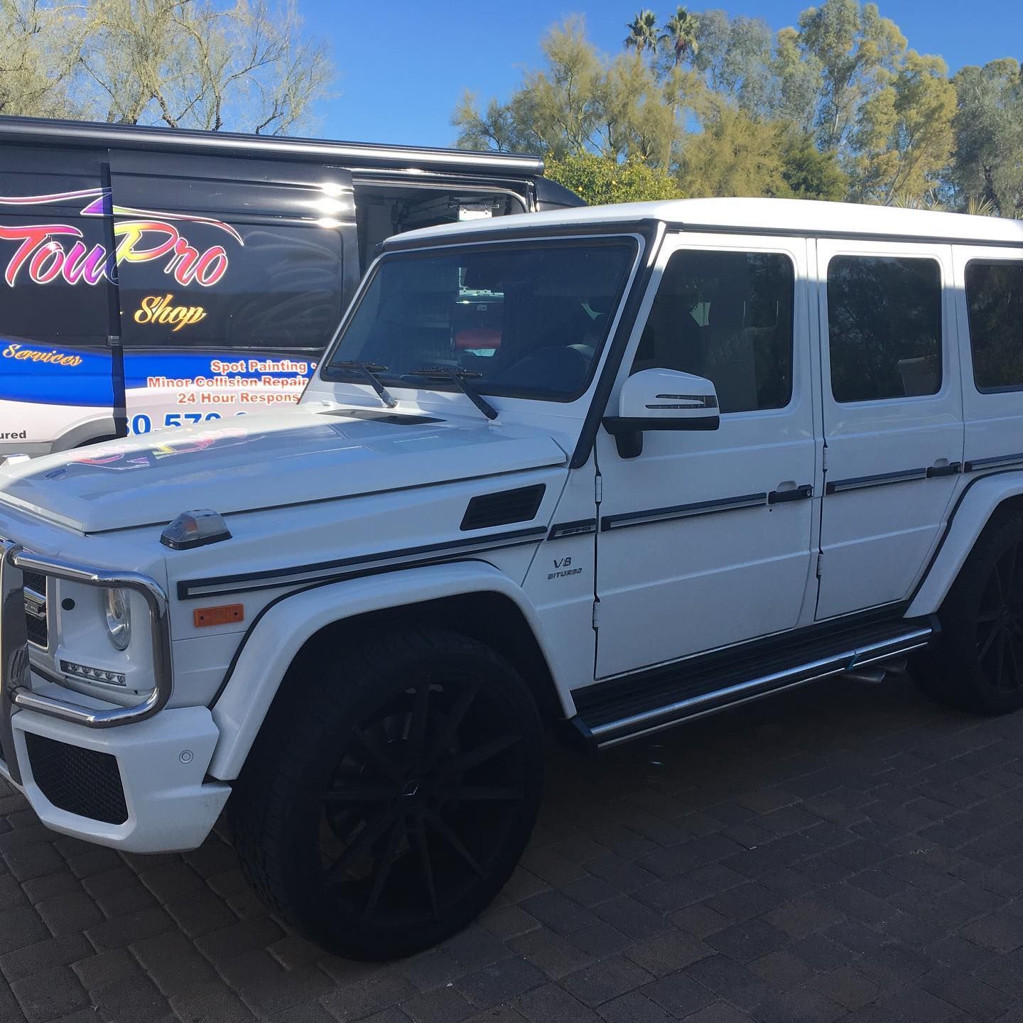 A white car raised on a hydraulic lift in a garage, missing its rear wheel.