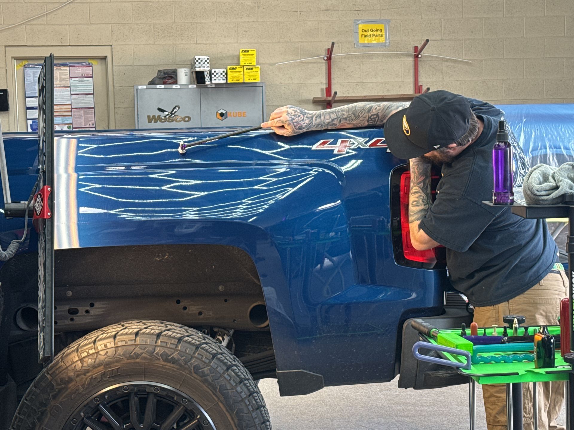 A person performs auto body repair on the blue rear panel of a pickup truck in a workshop.