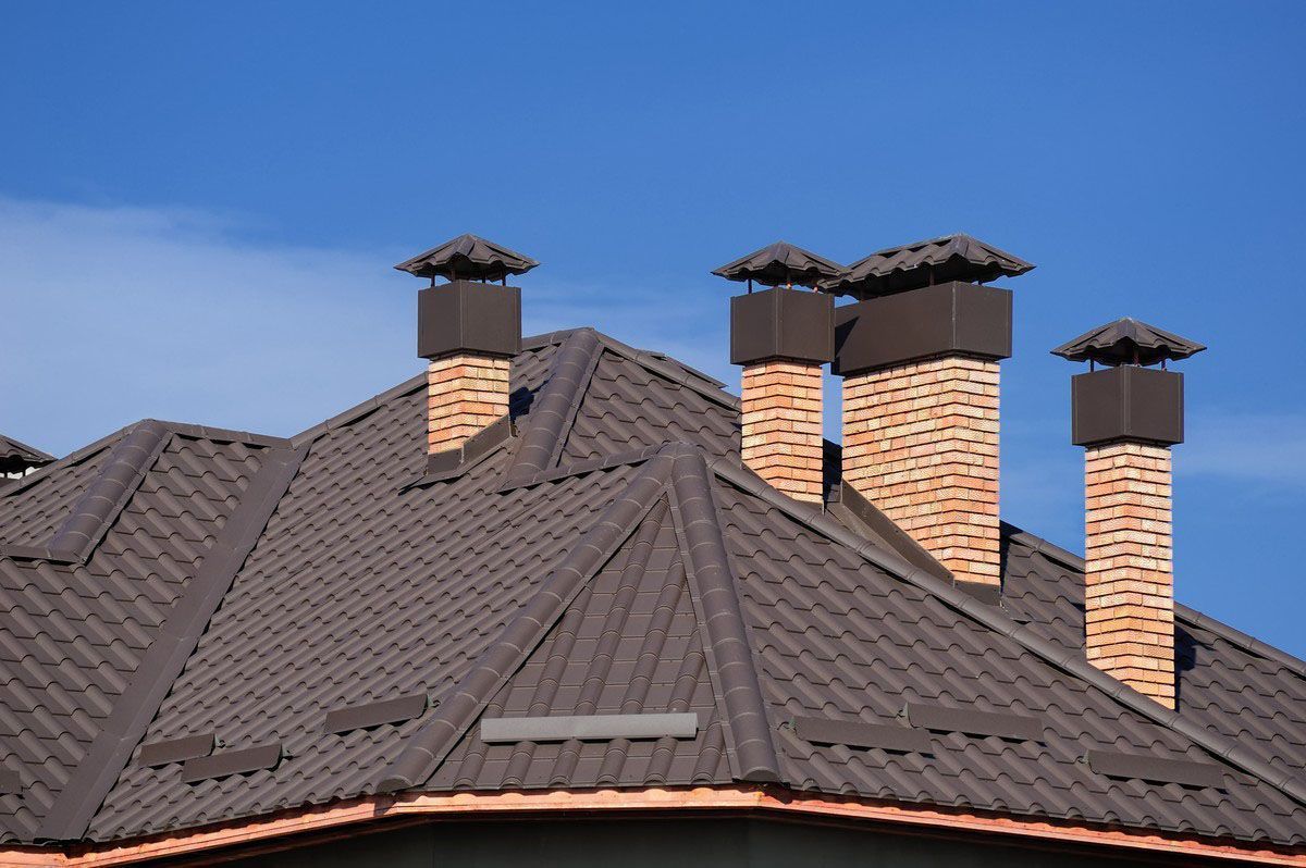 Brown roof with multiple brick chimneys against a blue sky.