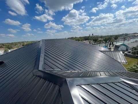 A black metal roof on a building with a blue sky and white clouds overhead.
