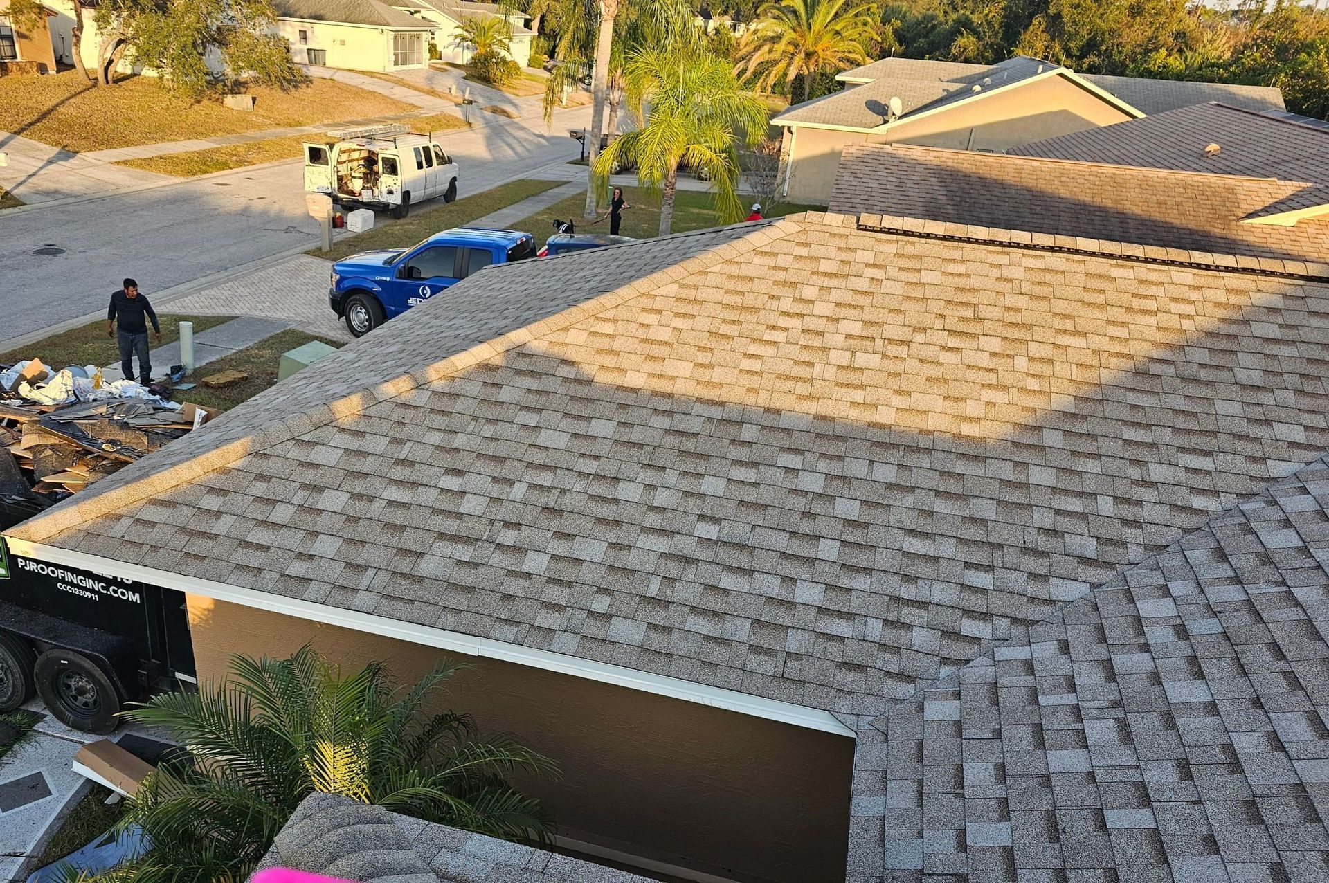 Rooftop with brown shingles; a blue car and white van parked on the street with workers.