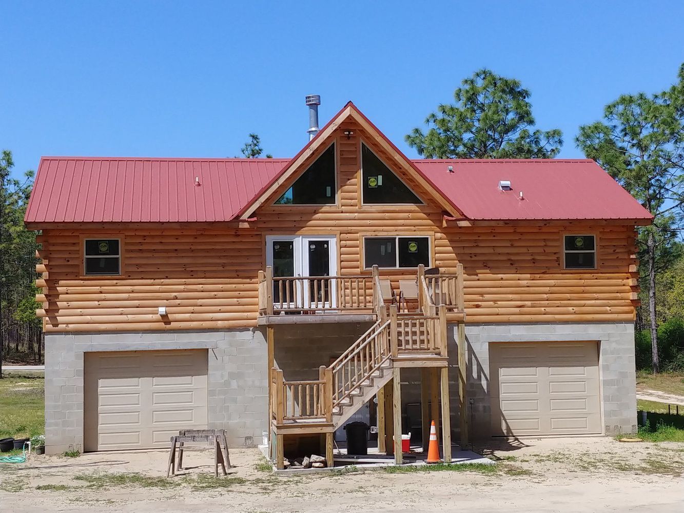 Log cabin house with red metal roof, built over a concrete garage with wooden staircase.