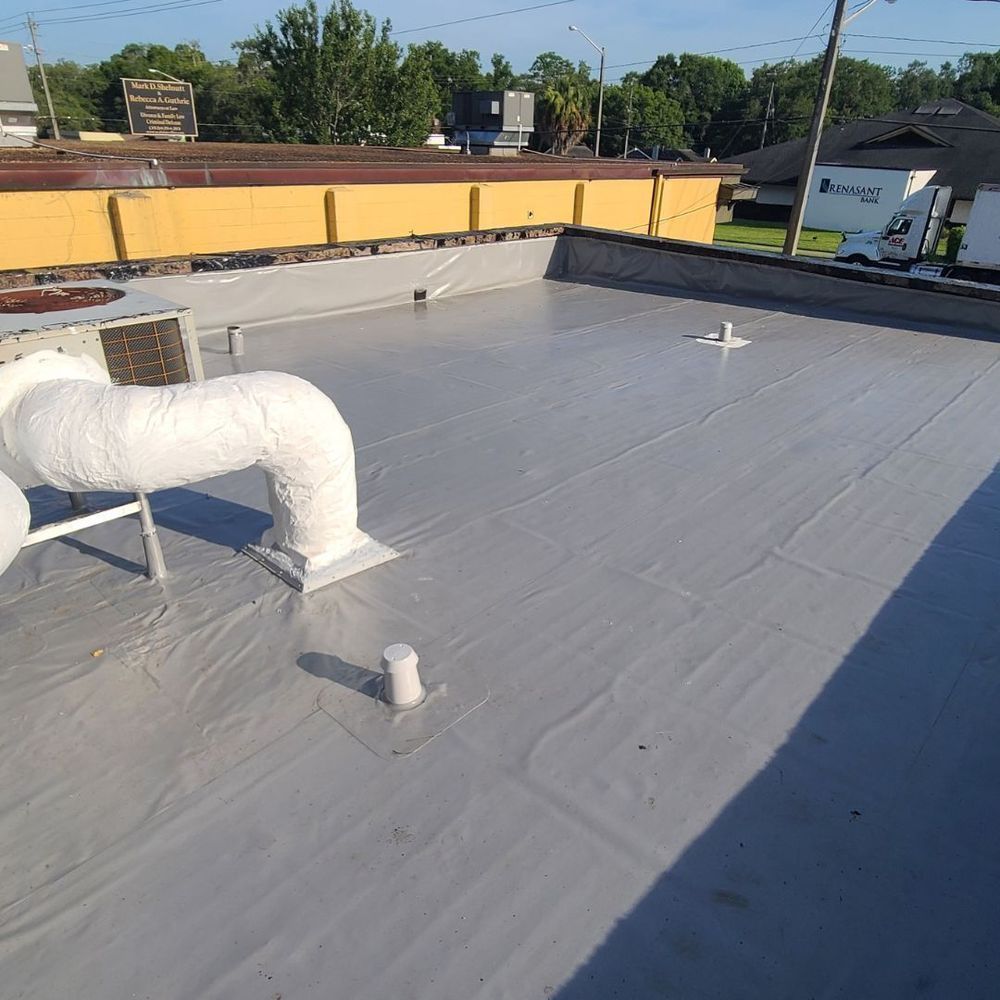 Flat, gray commercial roof with pipes and vents, in a daytime setting.