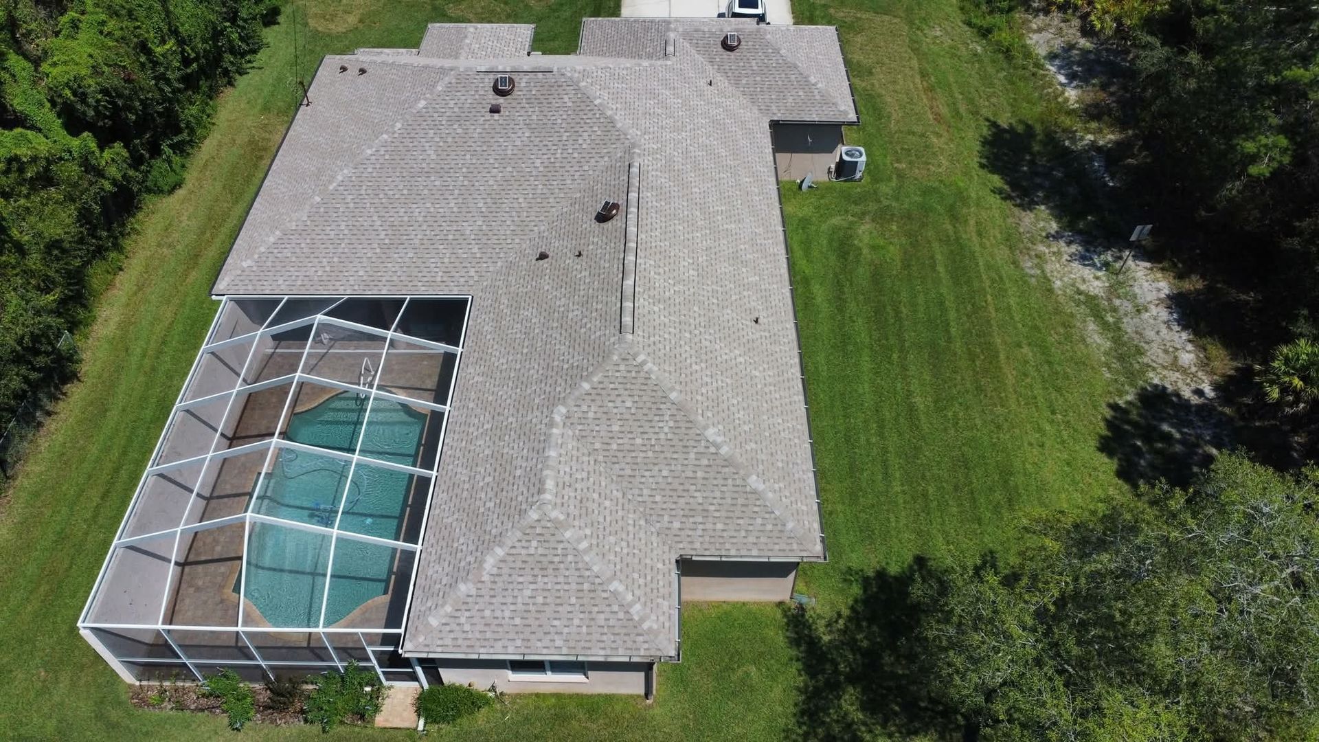 Aerial view of a house with a pool enclosed in a screen, surrounded by grass and trees.
