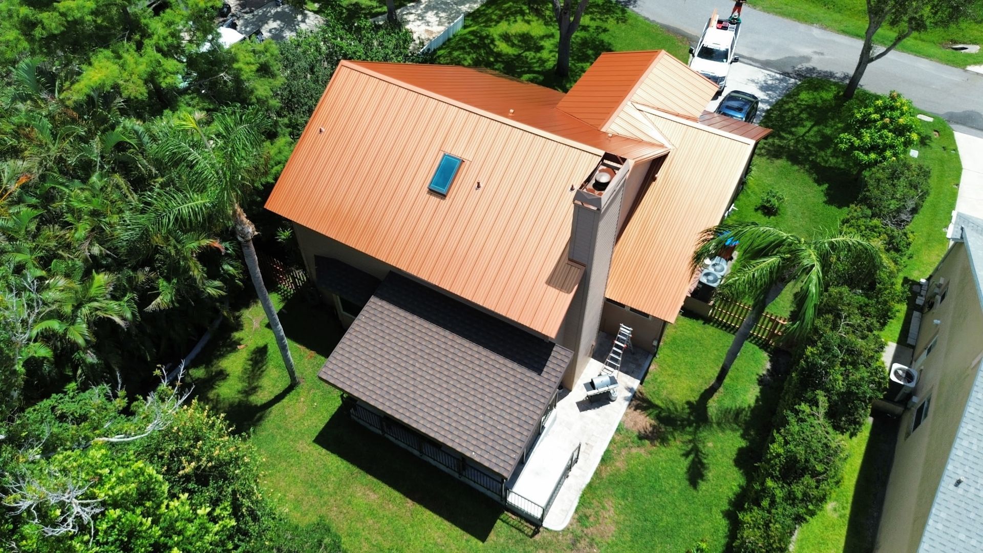 Aerial view of a house with a copper-colored roof, surrounded by green trees and grass.