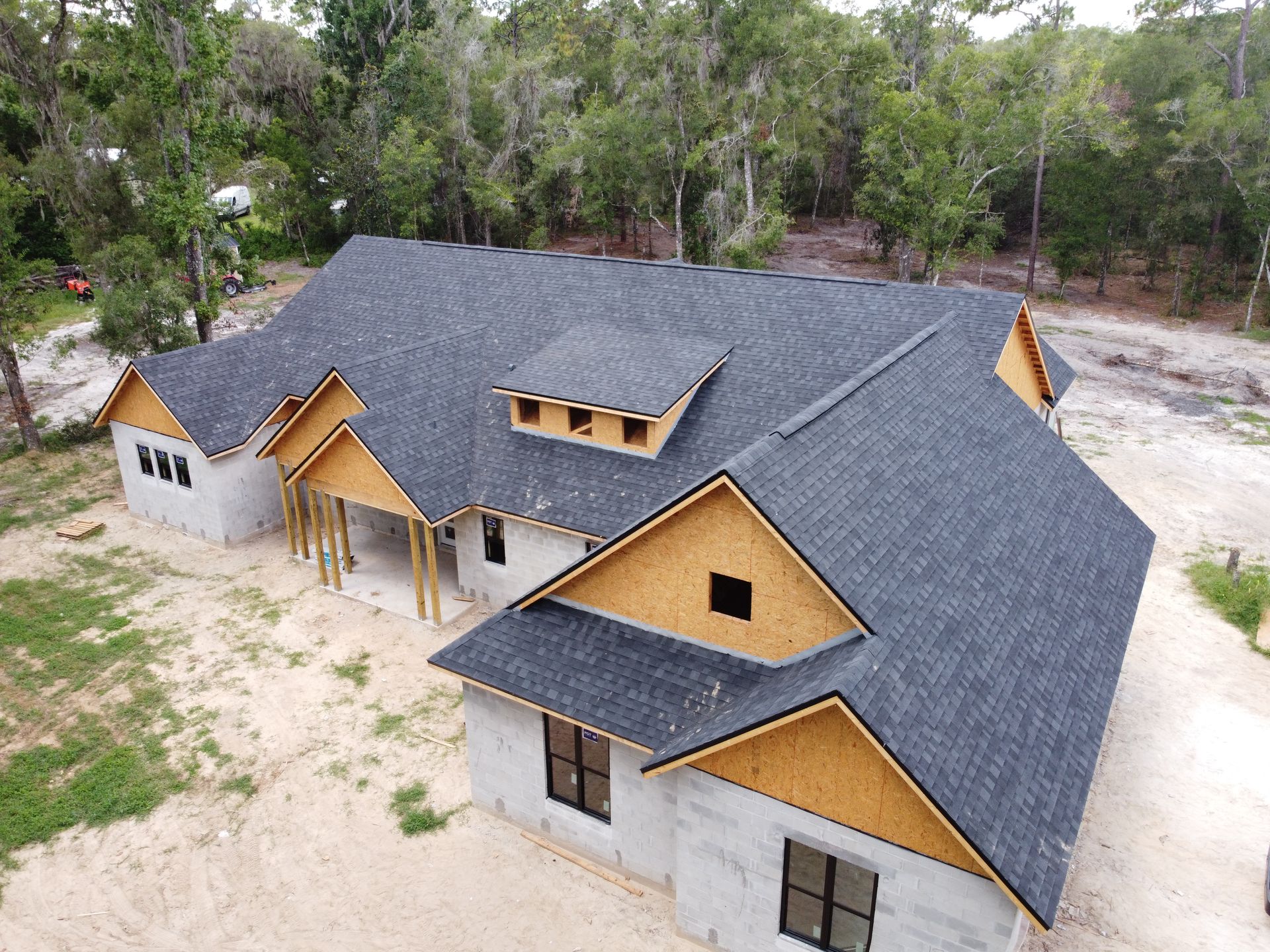 New house under construction with a dark gray shingle roof, unfinished walls, and wooden accents, outdoors.