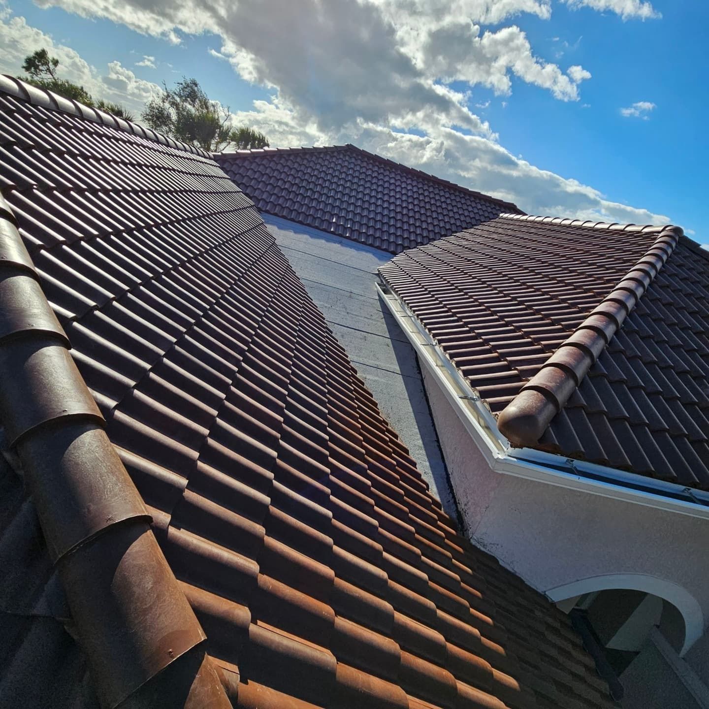 Brown tiled roof with blue sky and clouds in the background.