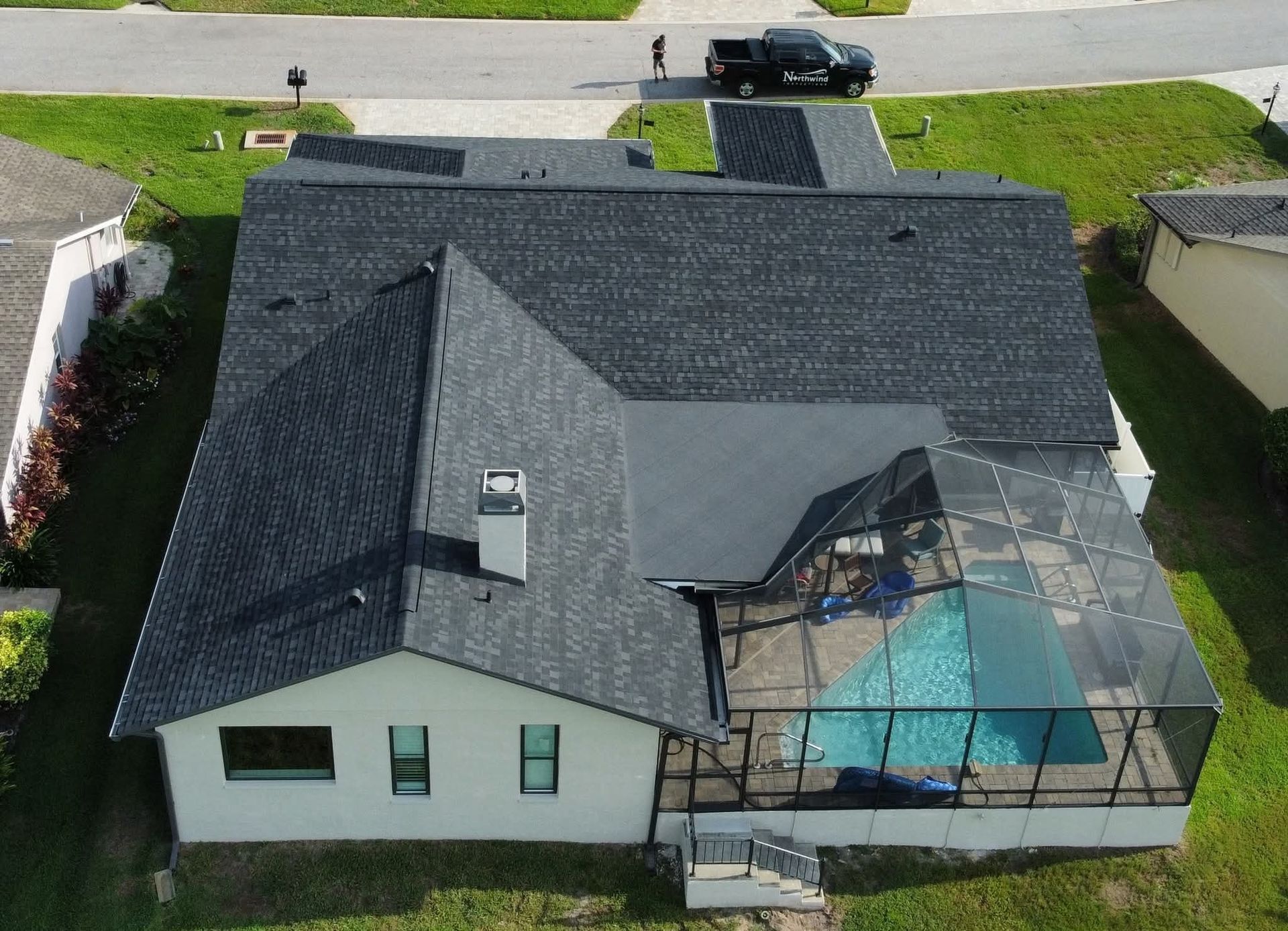 Aerial view of a house with a dark gray roof, a screened-in pool, and a black truck parked in the driveway.