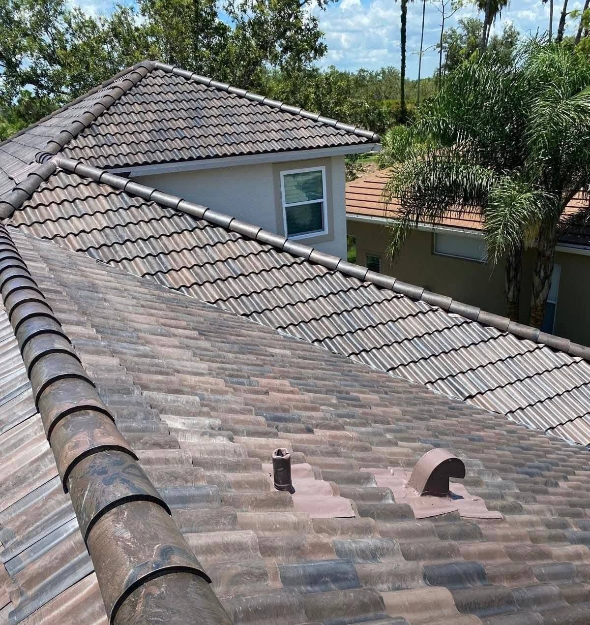 Close-up view of a tile roof, tan and brown tiles, with vents and a surrounding wooded area.