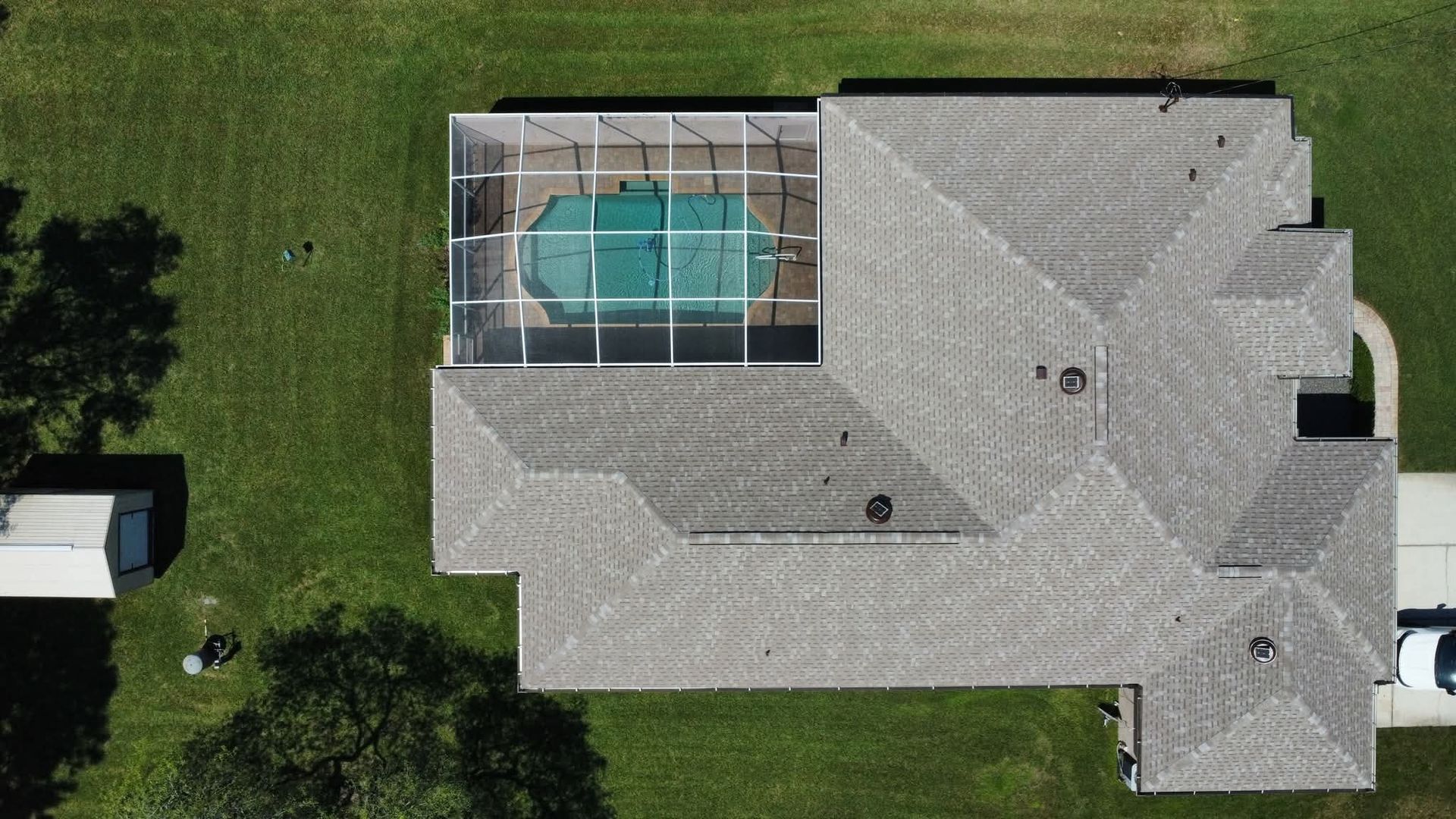 Aerial view of a gray-roofed house with a screened-in pool on green grass.