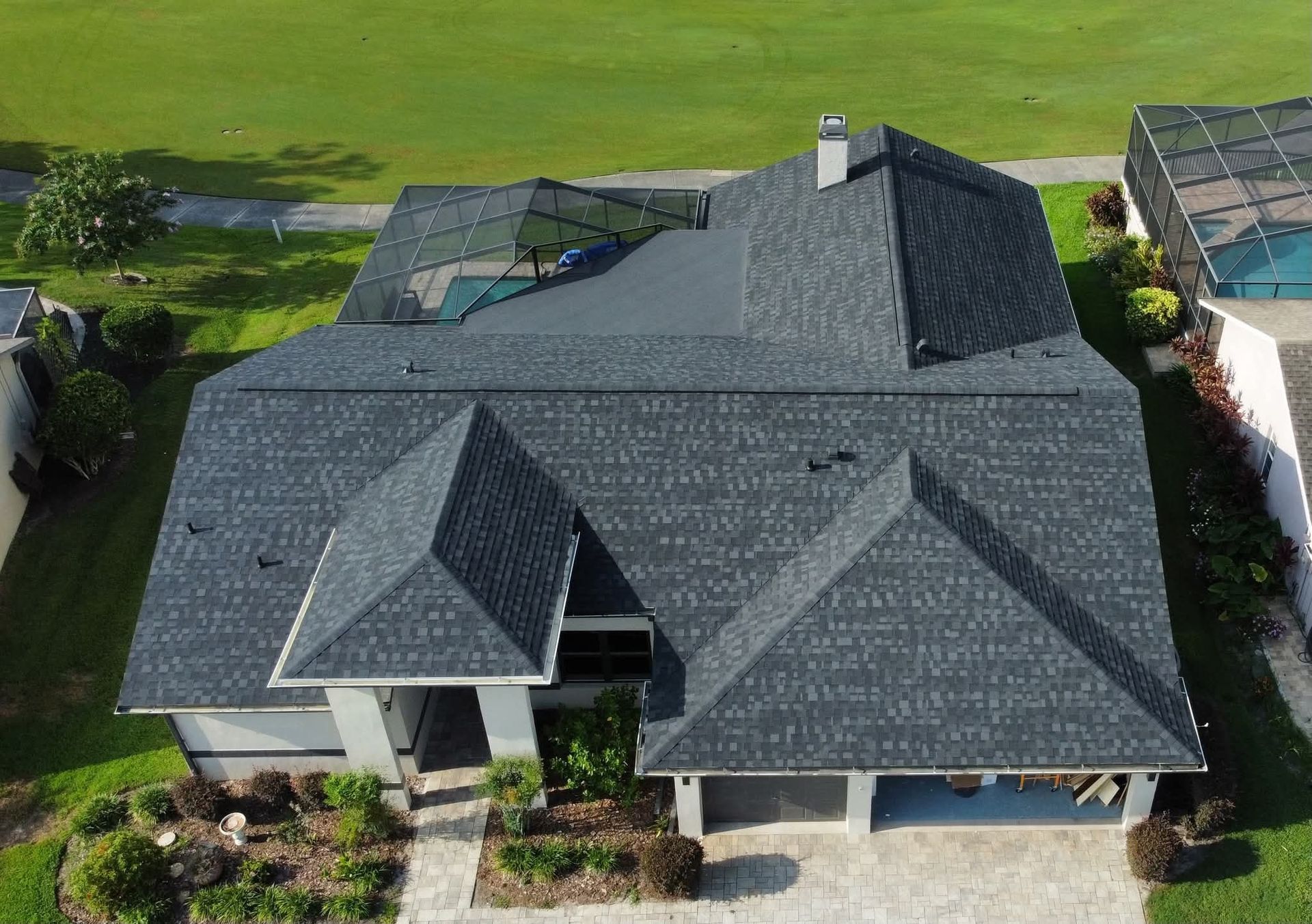 Aerial view of a house with a dark gray shingle roof, pool, and green lawn.