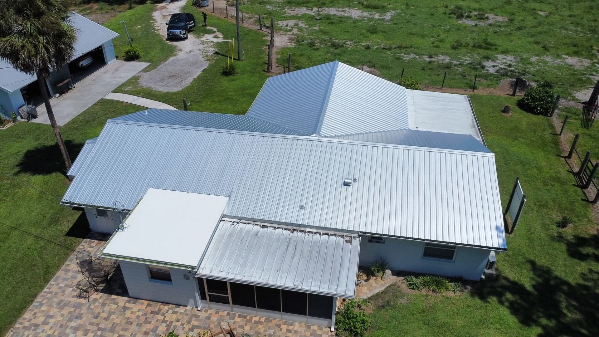 Aerial view of a white house with a metal roof surrounded by green grass and a paved driveway.