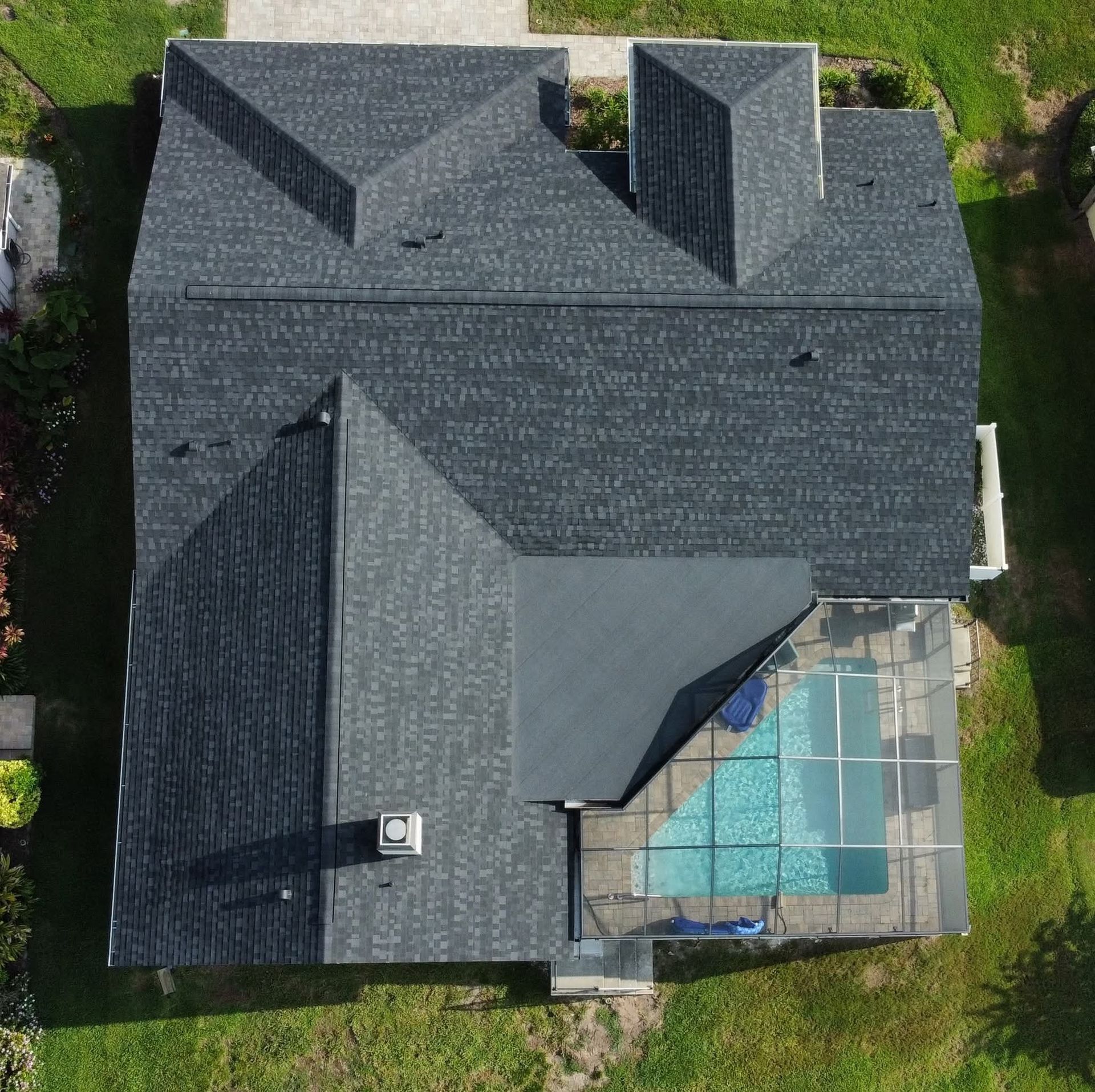 Overhead view of a house with a dark gray roof, a pool, and surrounding green grass.