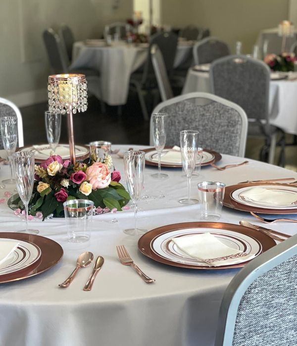 A table set for a wedding reception with plates , glasses , silverware and a candle in the middle.