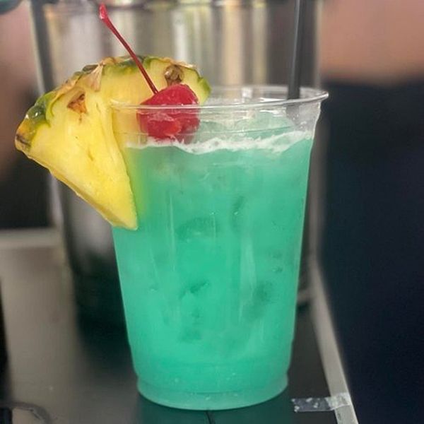 A blue drink with a pineapple slice and a cherry on top.