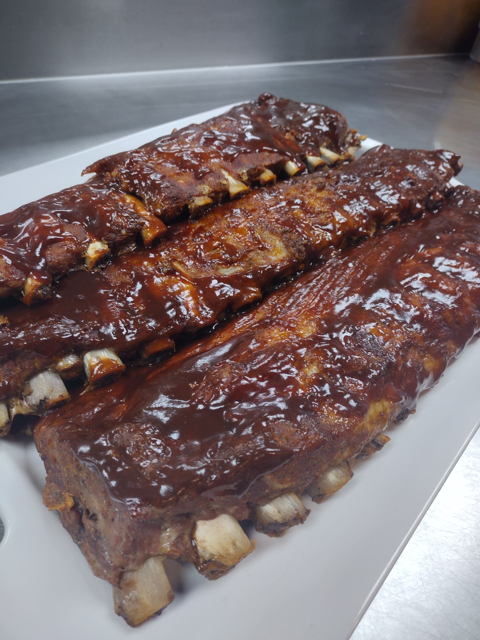 A white plate topped with ribs covered in barbecue sauce.