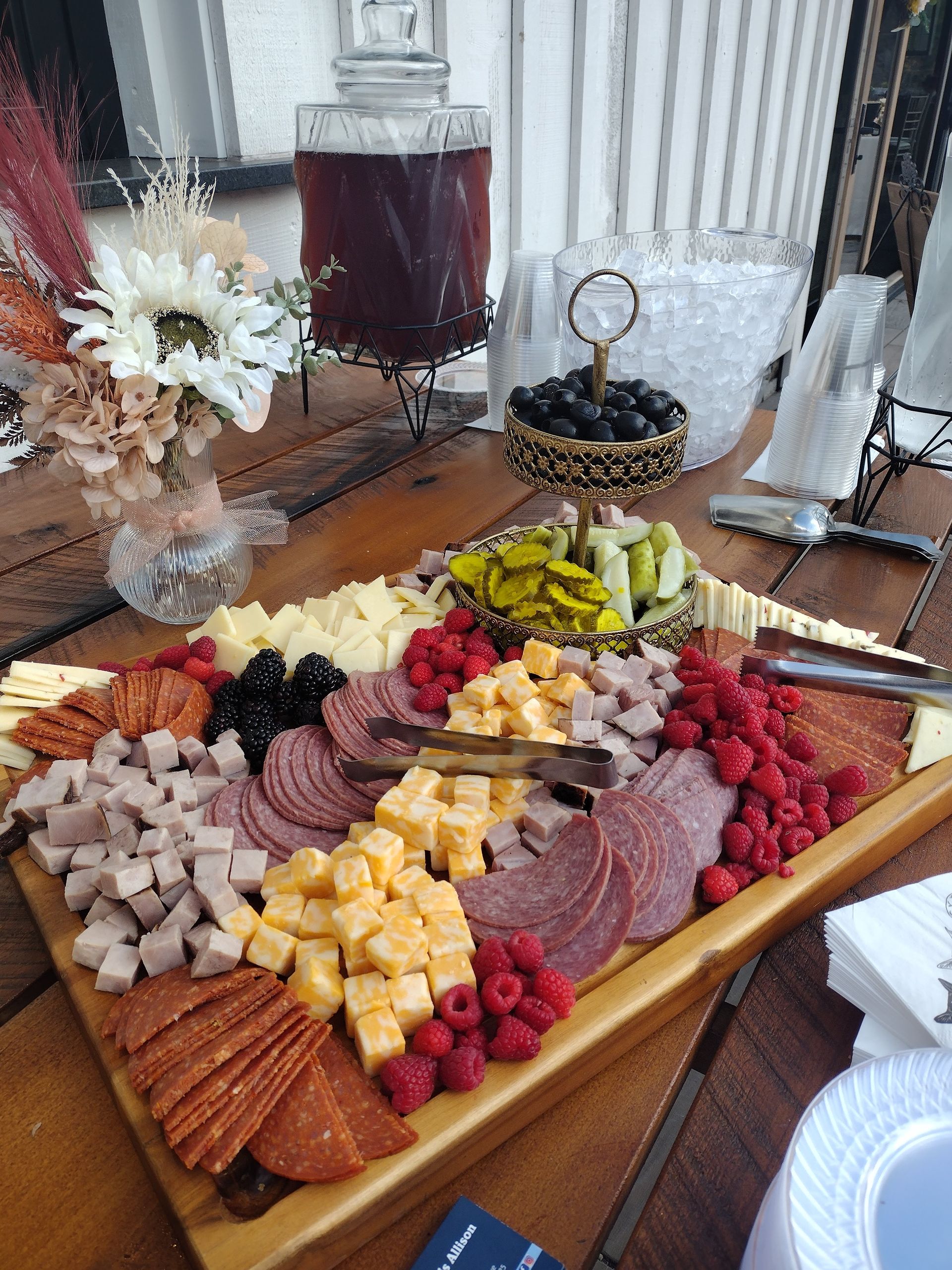 A wooden cutting board filled with meats , cheeses , raspberries , and olives.