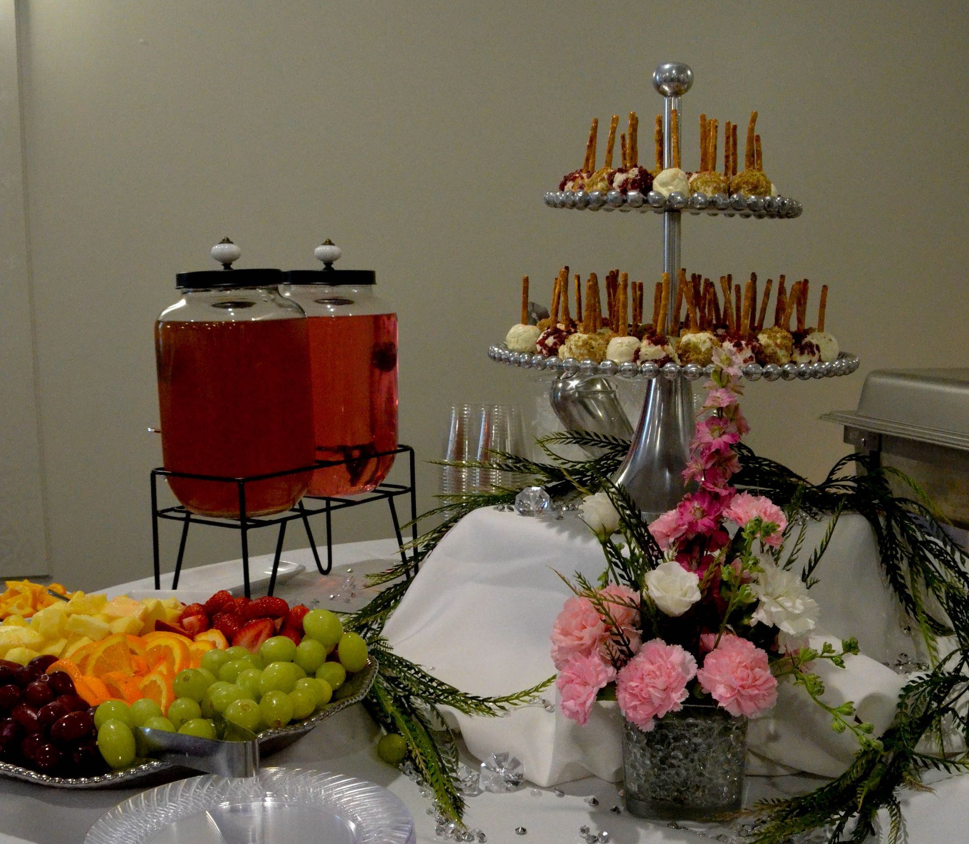 A table with a display of fruit and flowers and a drink dispenser