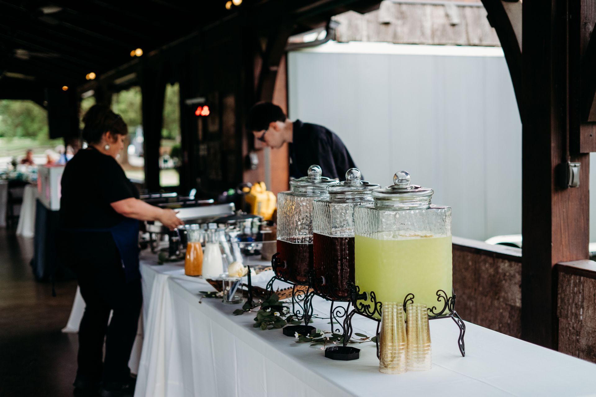 A man and a woman are serving drinks at a buffet table.