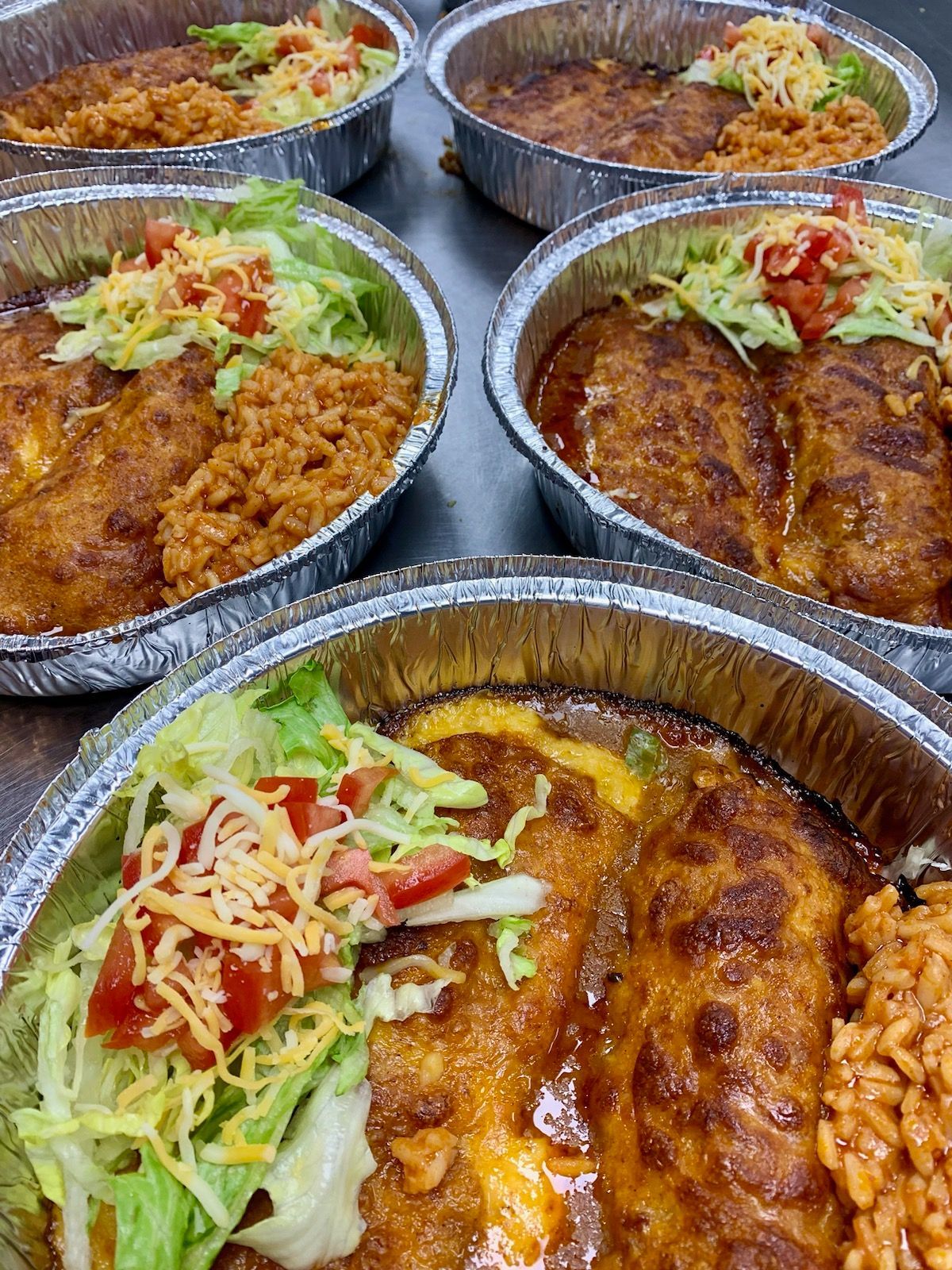 A bunch of foil containers filled with mexican food on a table.