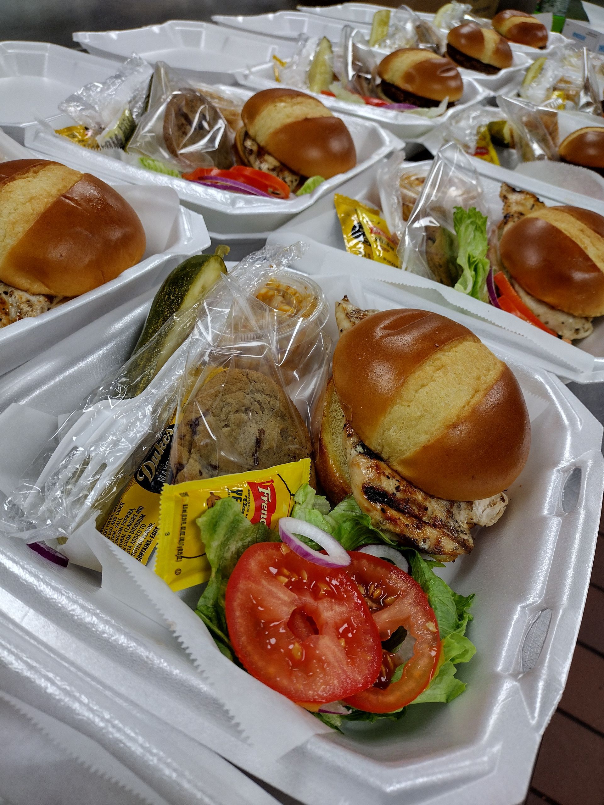 A bunch of styrofoam containers filled with hamburgers and vegetables