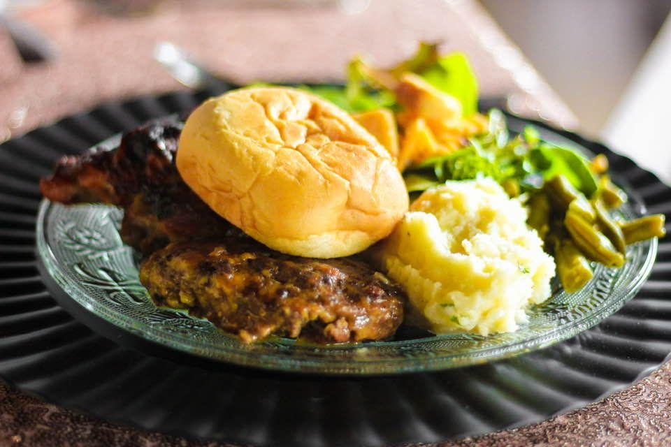 A plate of food with mashed potatoes , green beans and a hamburger on a table.