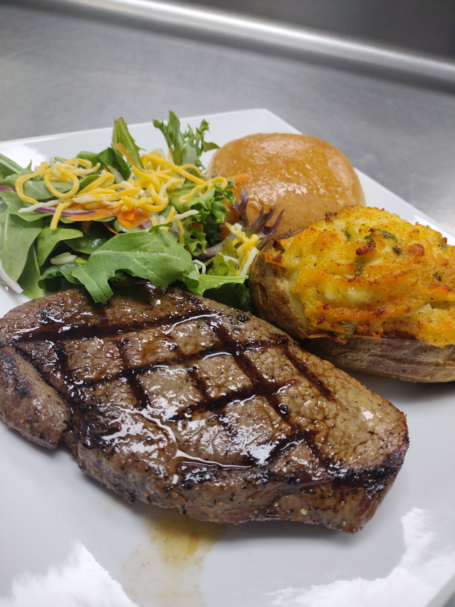 A white plate topped with a steak potatoes and a salad