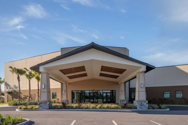 Front entrance of a modern building with a peaked canopy, glass doors, and palm trees outside