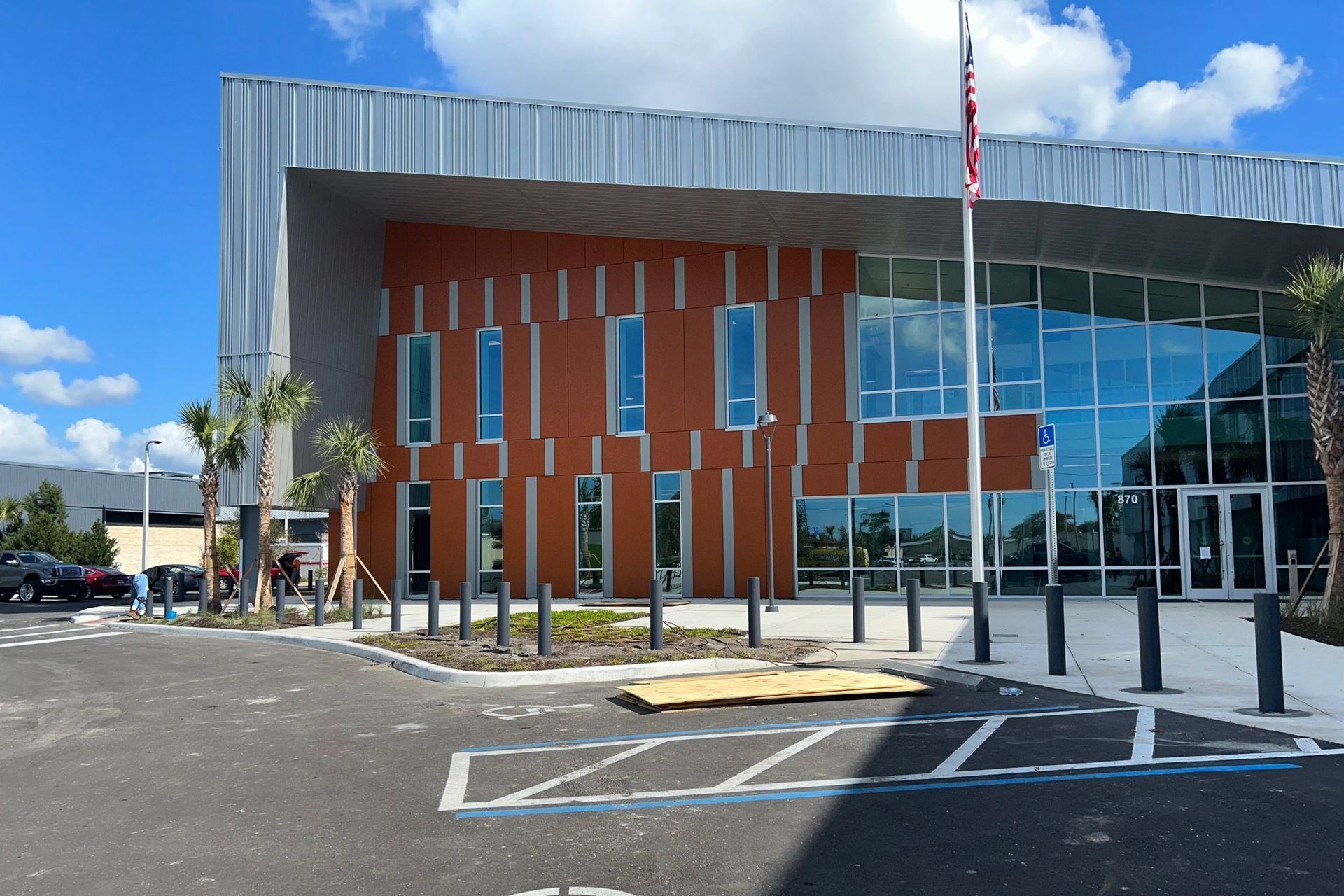 Modern building exterior with glass entrance, red paneling, and a parking lot in front