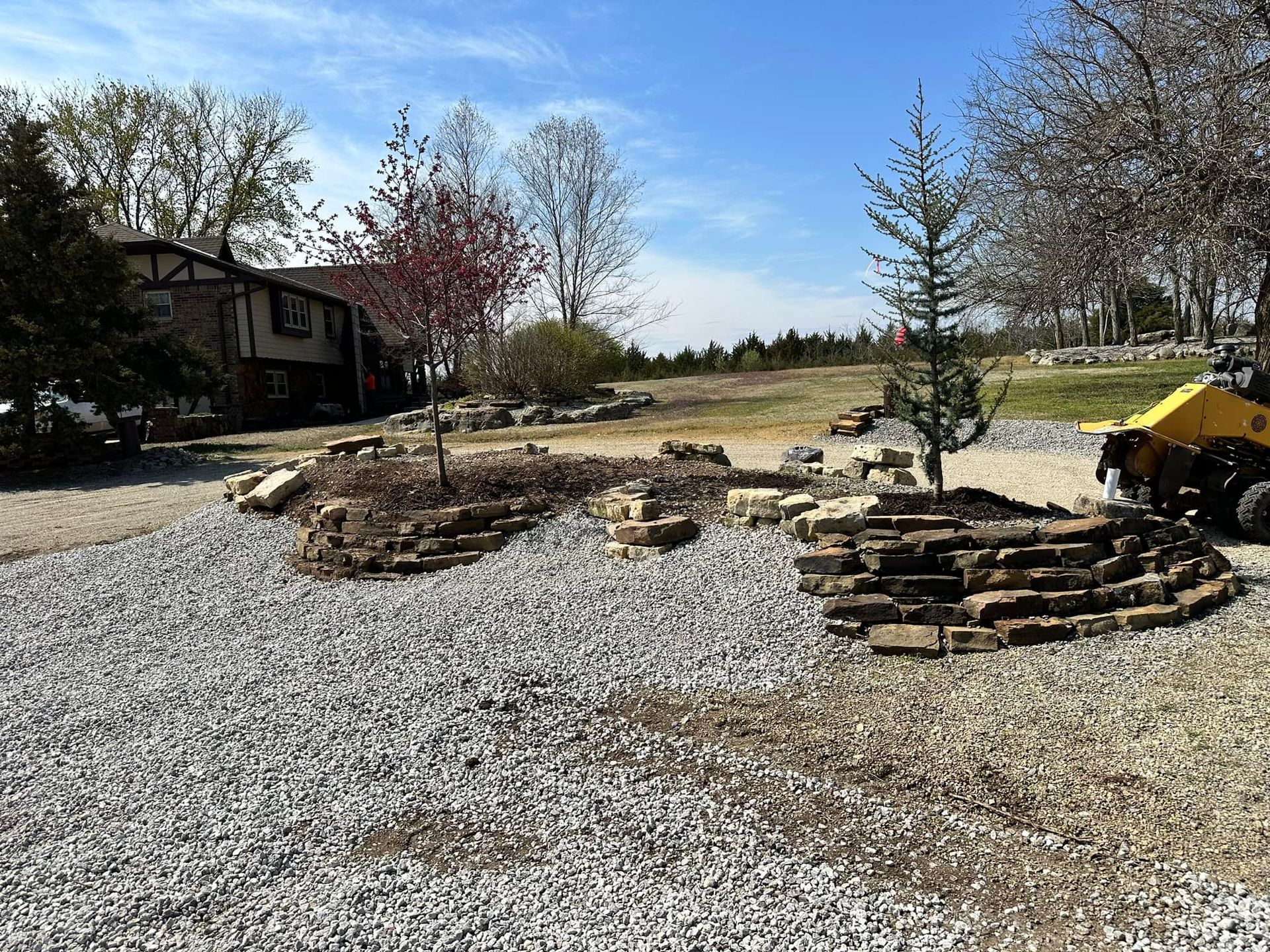 A yellow truck is parked in a gravel driveway in front of a house.