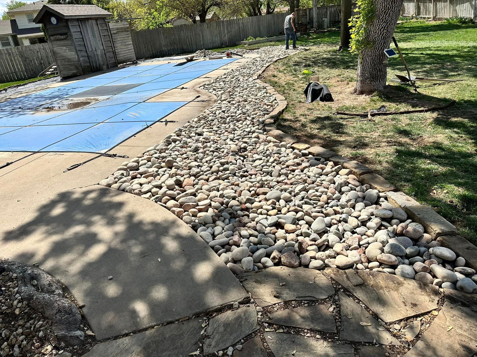 A stone walkway leading to a pool with a blue cover on it.
